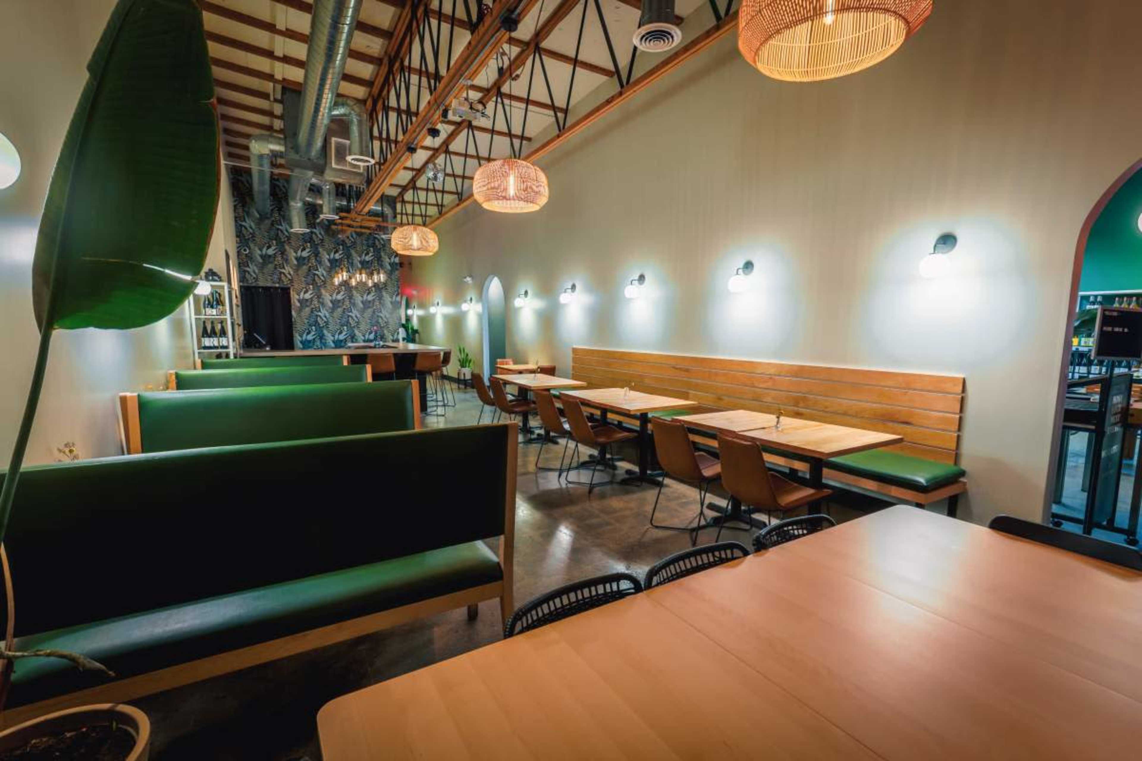 The image shows a modern restaurant interior with green booth seating, wooden tables, and decorative lighting fixtures along the walls.