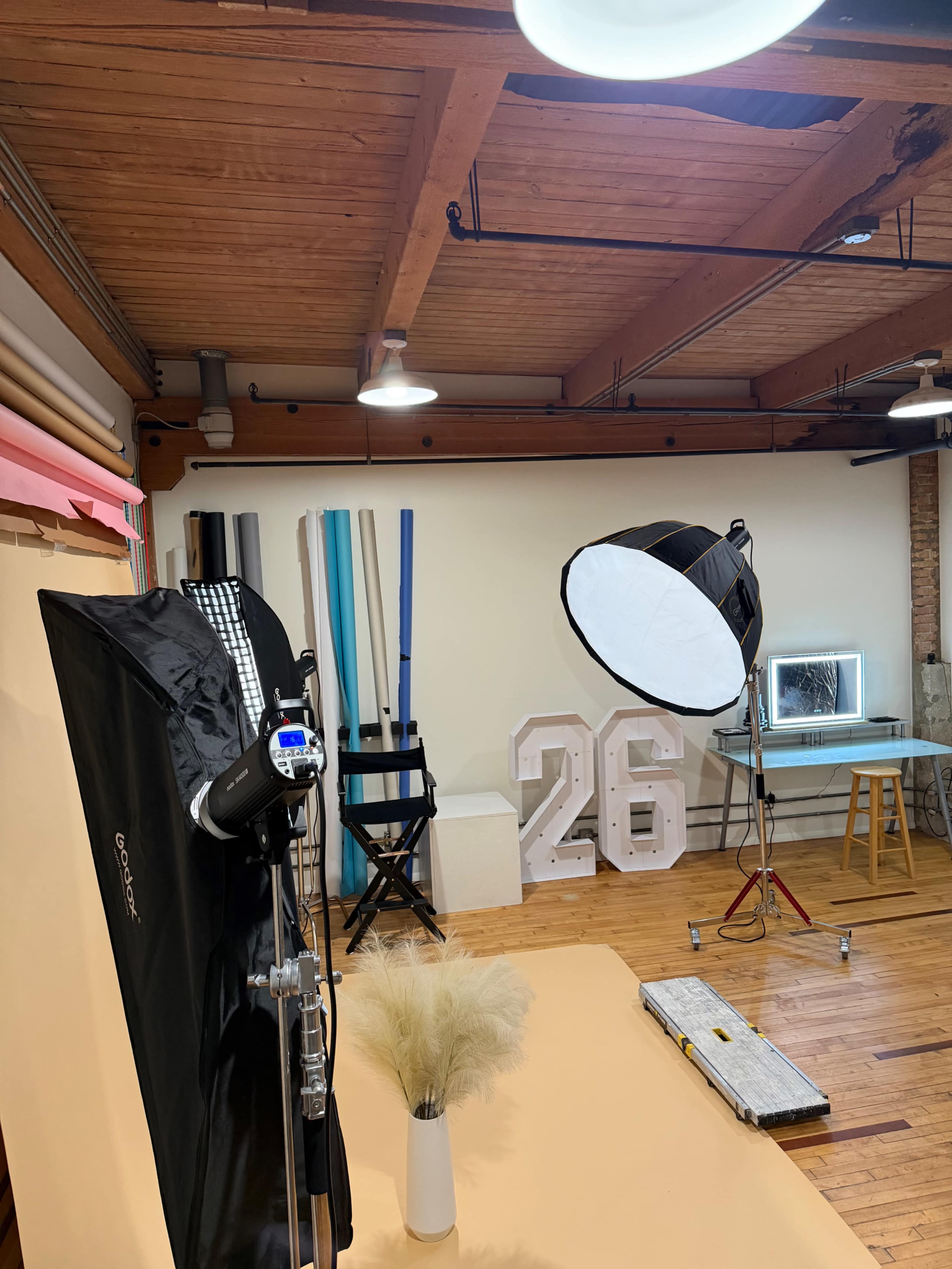 The image shows a photography studio with a backdrop setup, lighting equipment, a large decorative number "26," and various props arranged in the space.