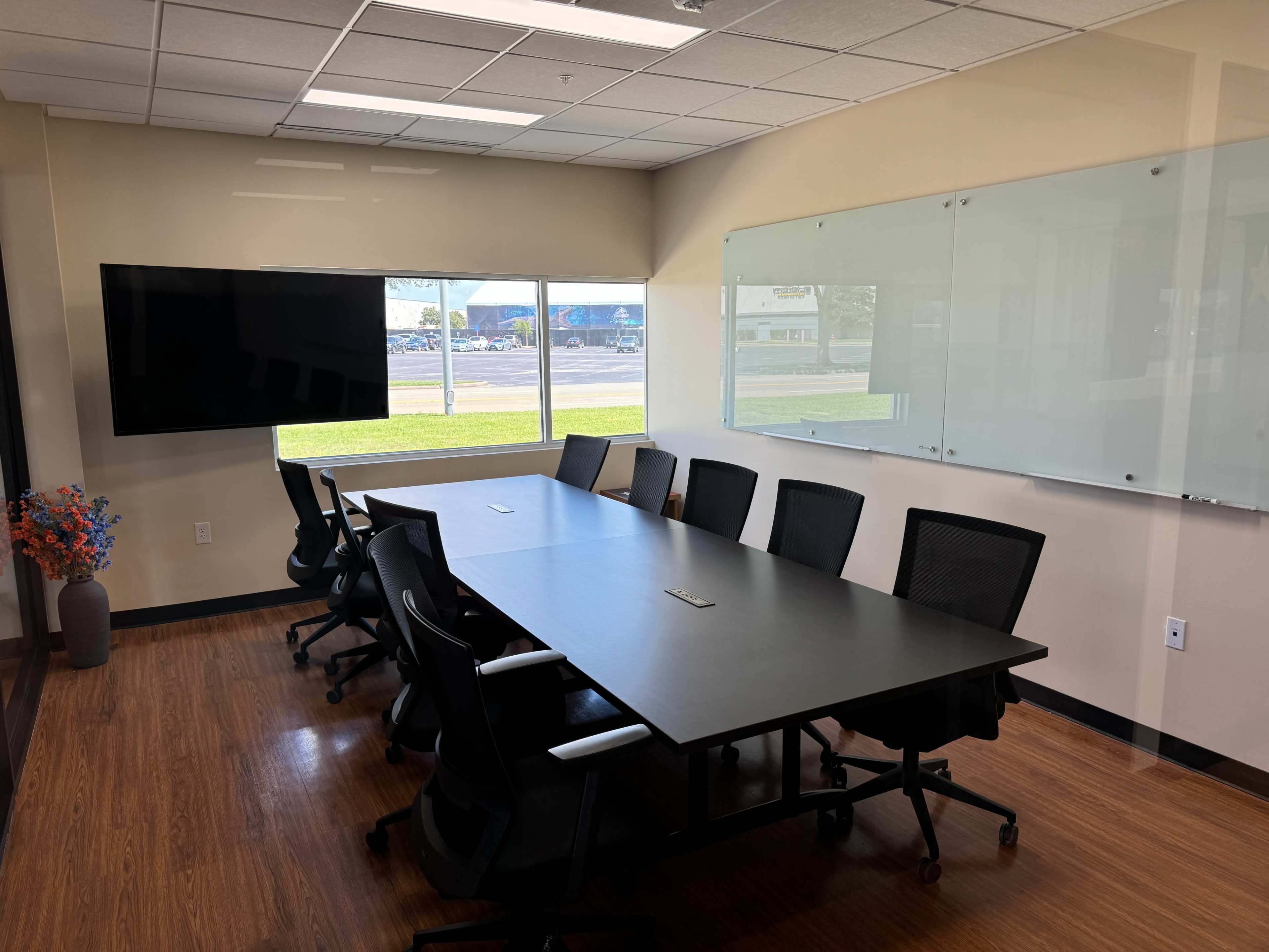 A modern conference room with a long table, several black chairs, a large screen on the wall, and whiteboards.