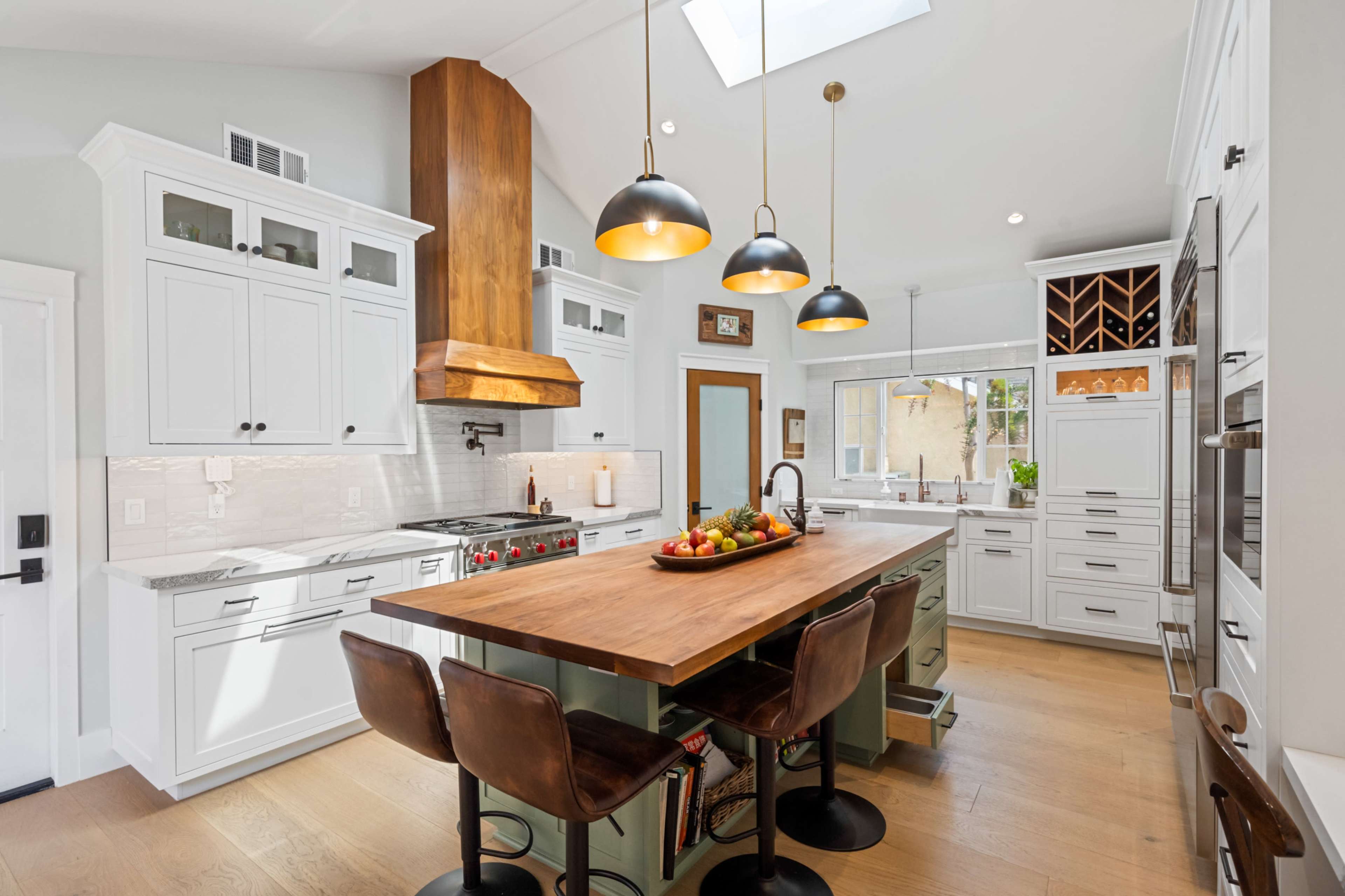 The image shows a modern kitchen featuring white cabinetry, a large wooden island with bar stools, and a skylight providing natural light.