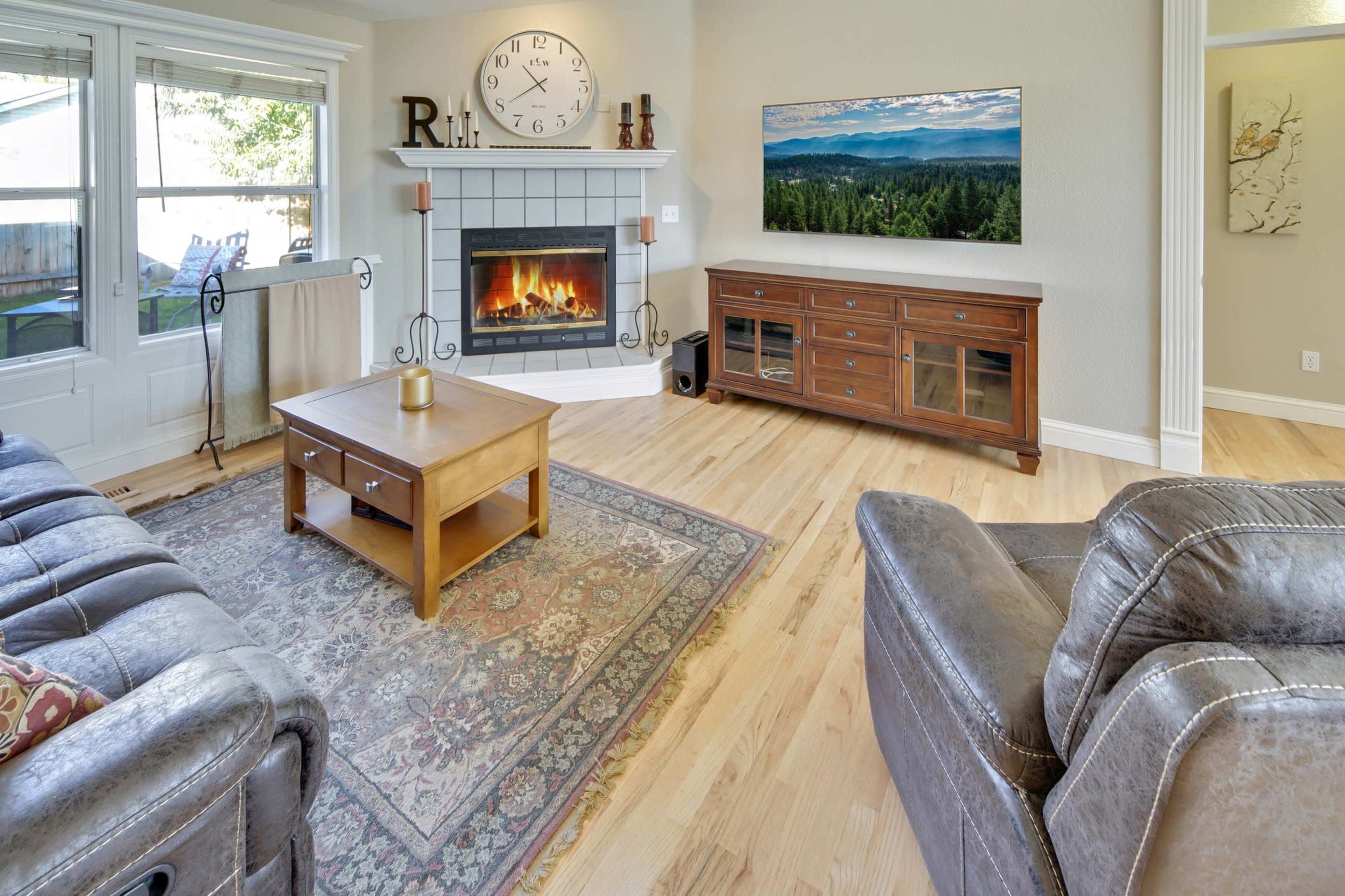 The living room features a gray fireplace with a wooden mantel, a coffee table in front, and a large television mounted on the wall above a wooden console.