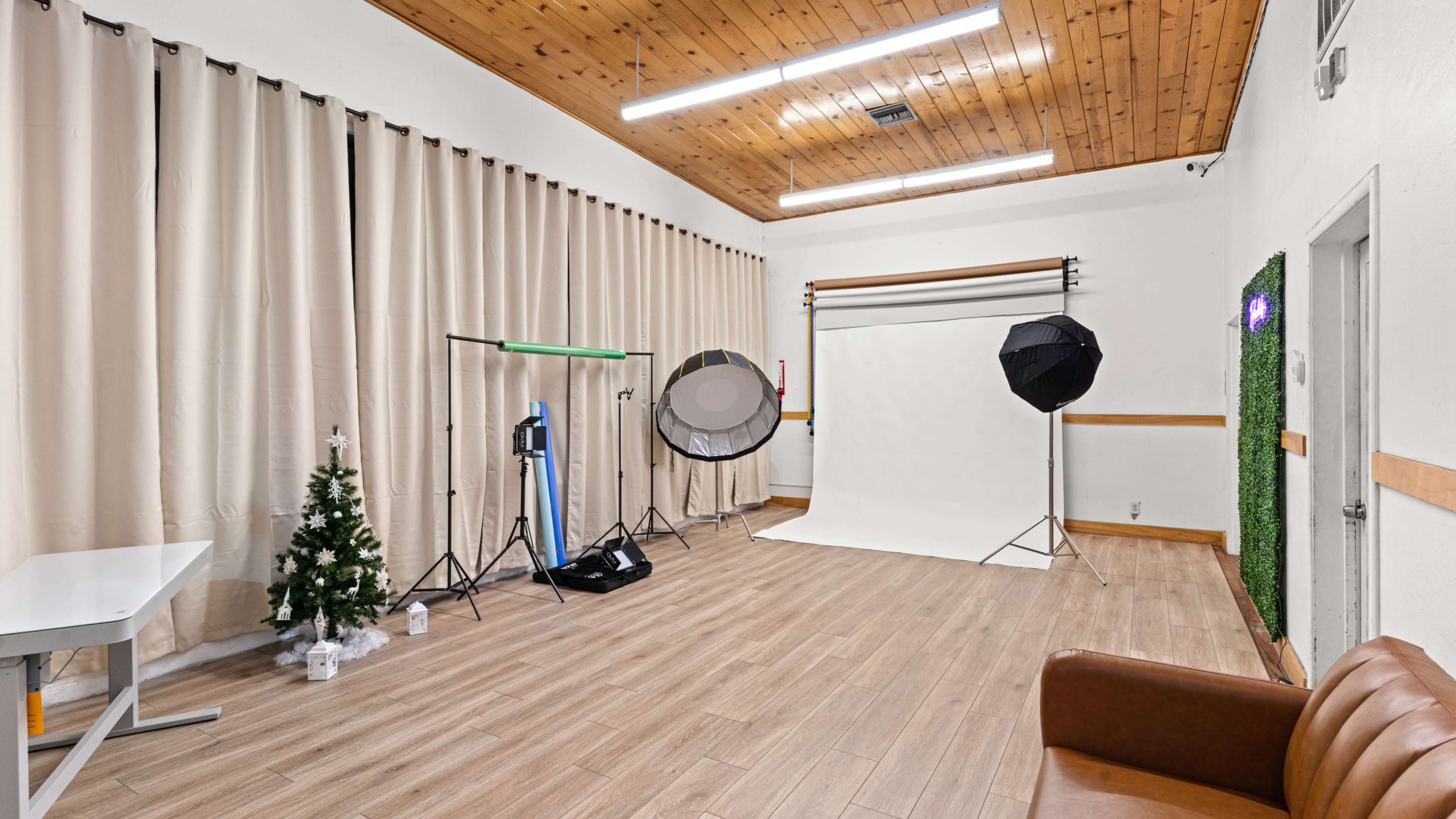 The image shows a photography studio with a white backdrop, lighting equipment, a small Christmas tree, and a brown couch.