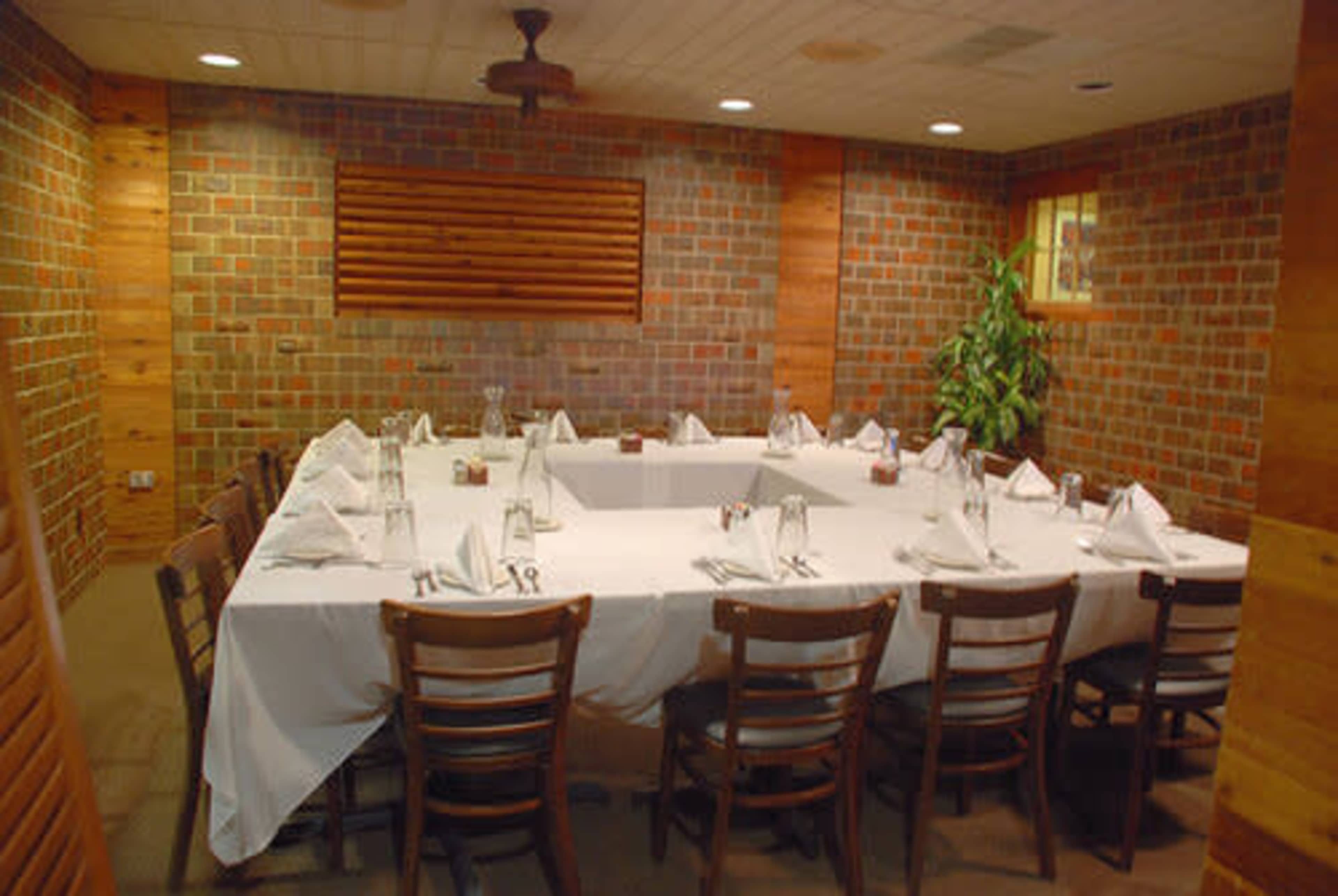 A private dining room with a rectangular table set with white tablecloth and napkins, surrounded by wooden chairs and featuring brick walls.