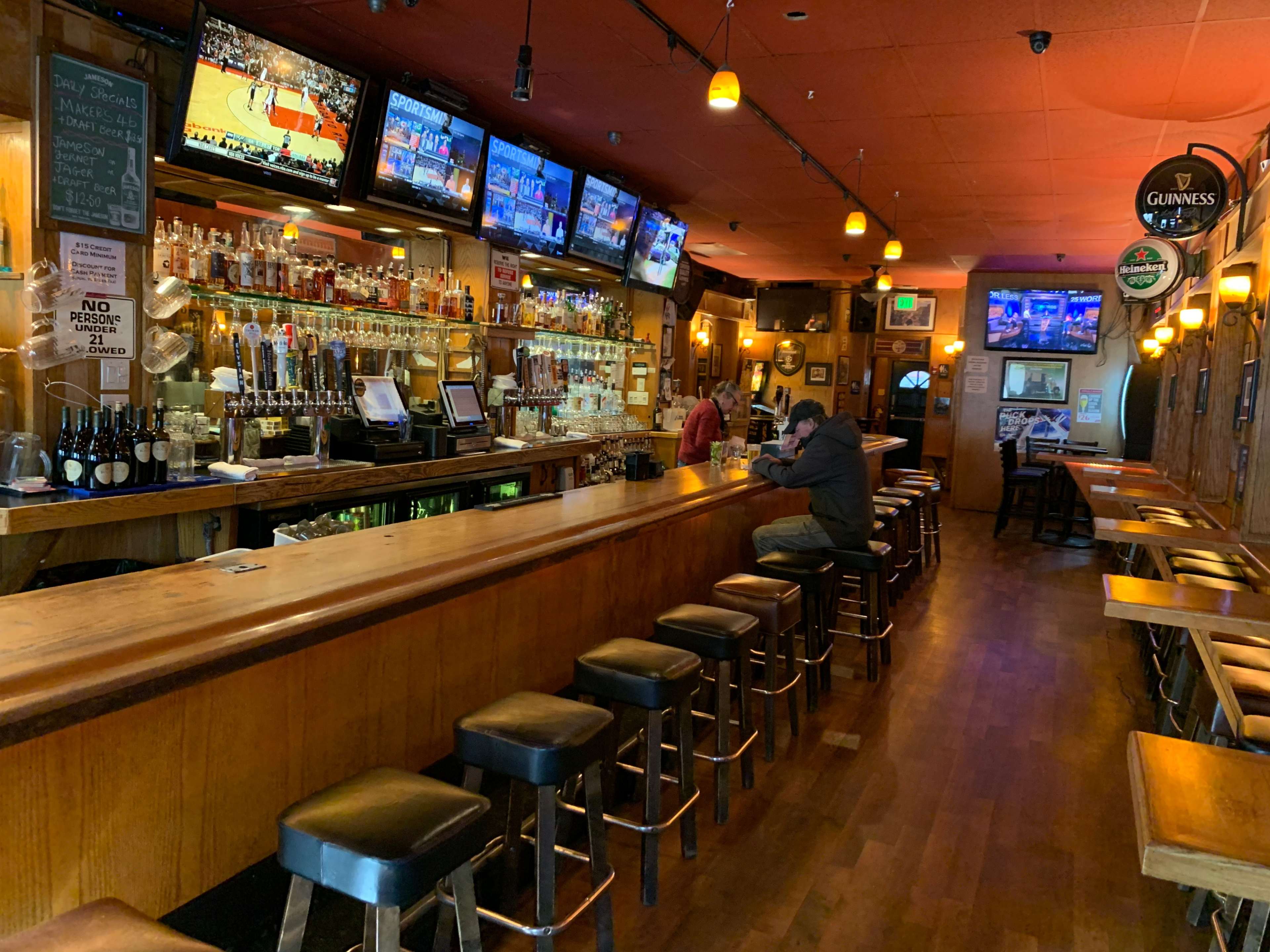 A bar with a long wooden countertop, several high stools, and multiple television screens displaying sports events.