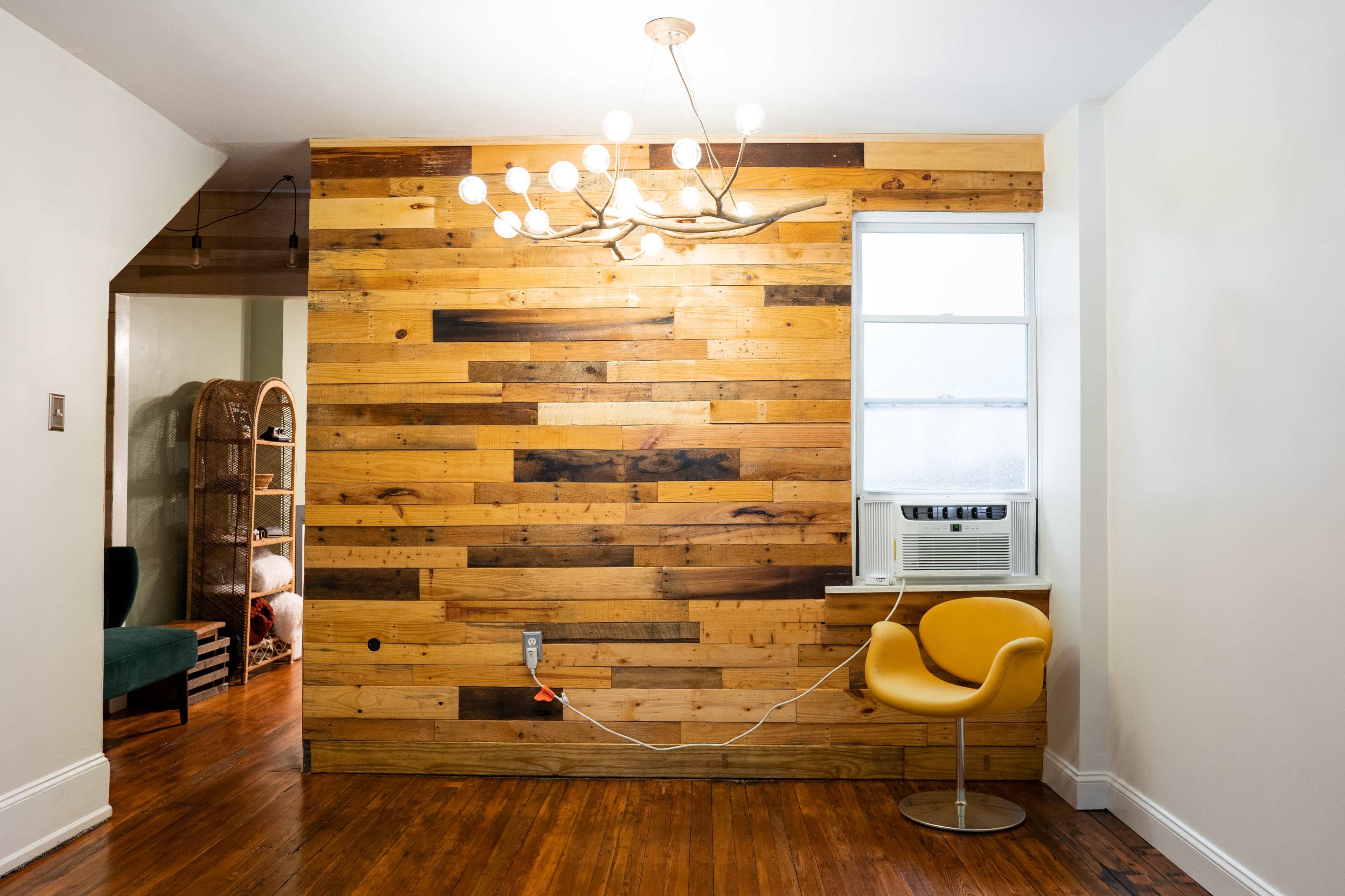A room with a wooden accent wall, a yellow chair, and an air conditioning unit underneath a window.