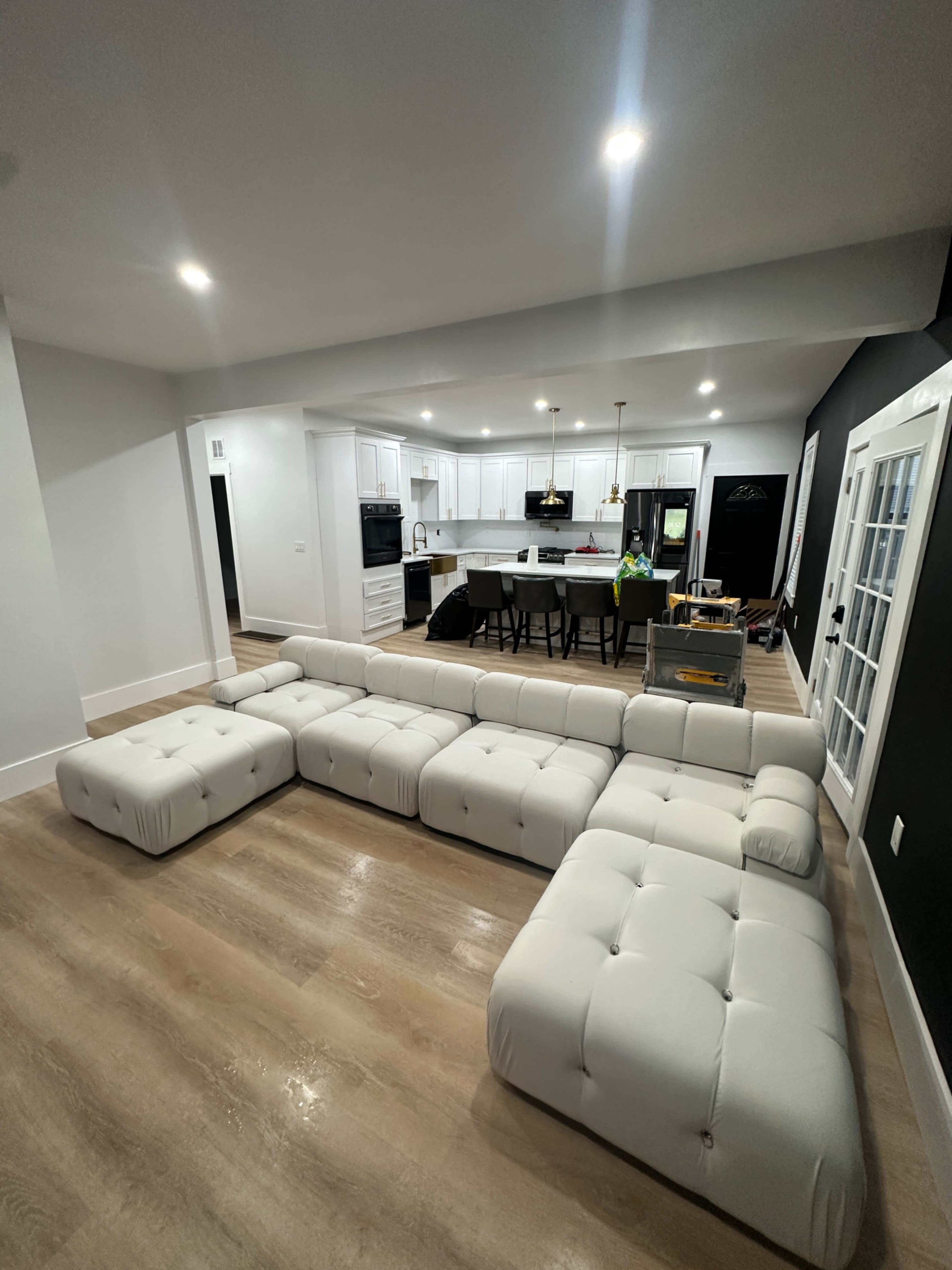 A white tufted sectional sofa is positioned in a modern, open-concept kitchen and living area.