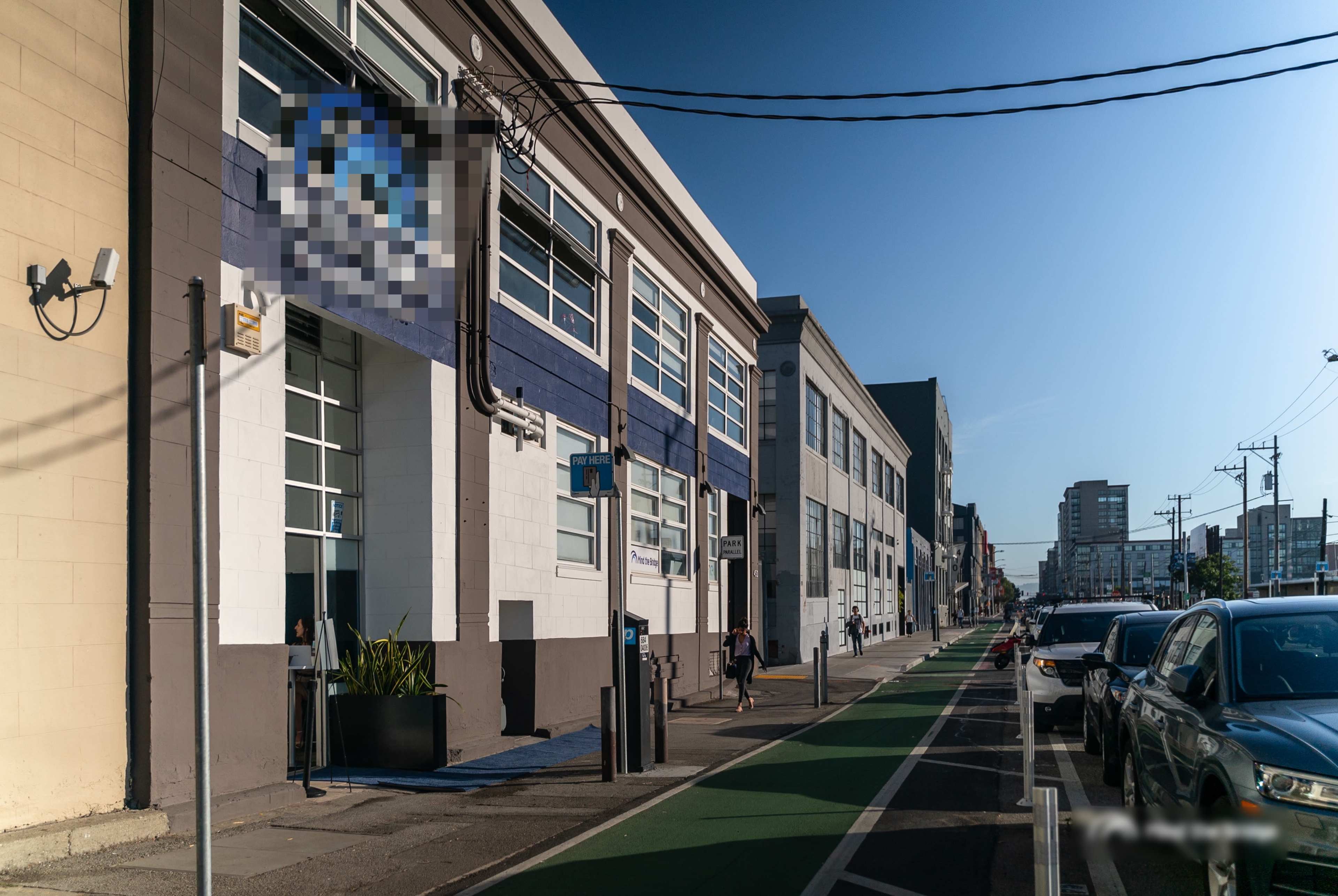 A modern building with large windows and a bike lane beside a street lined with parked cars.