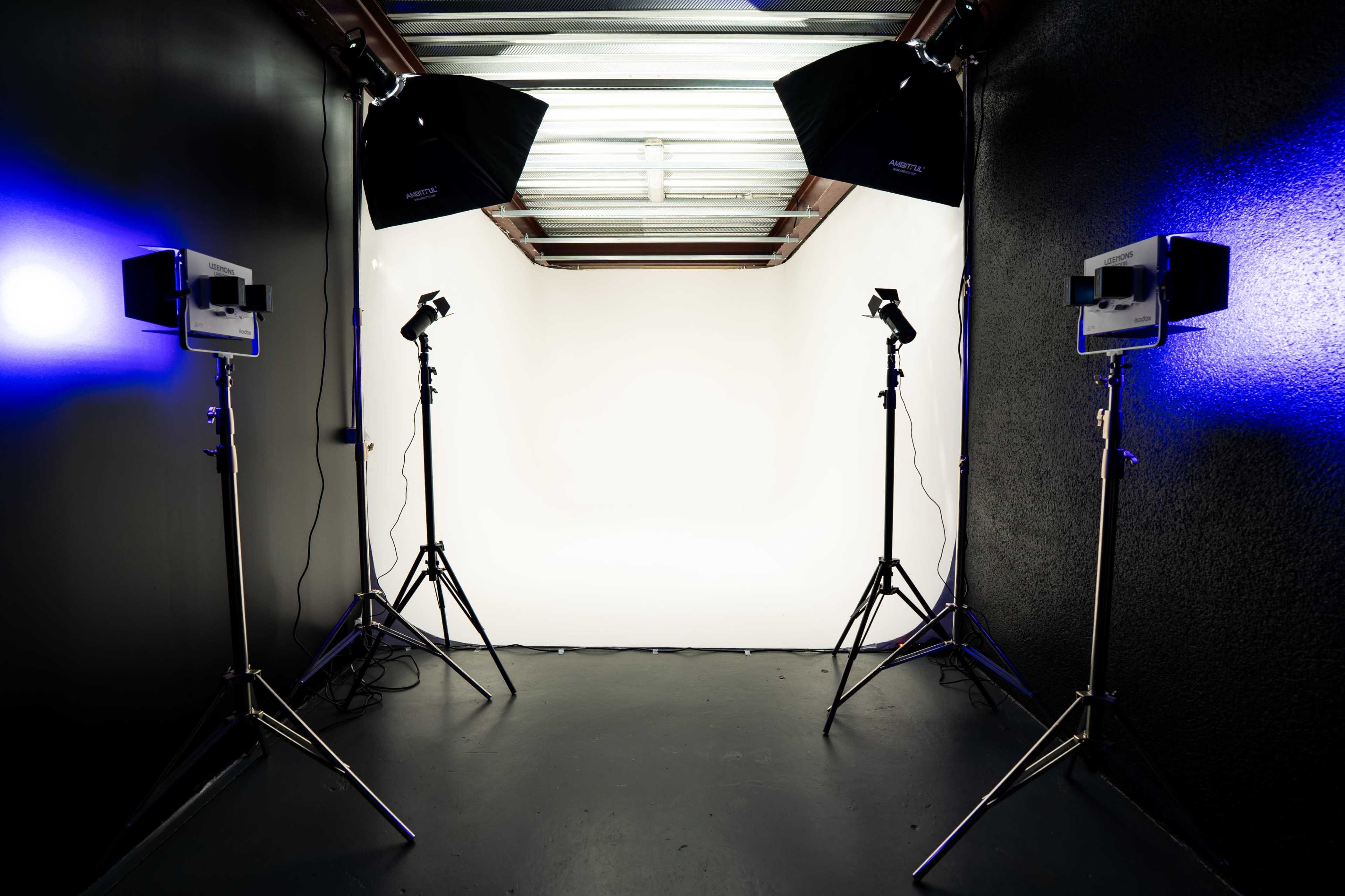 The image shows a photography studio setup with four lights on stands and a plain white backdrop.