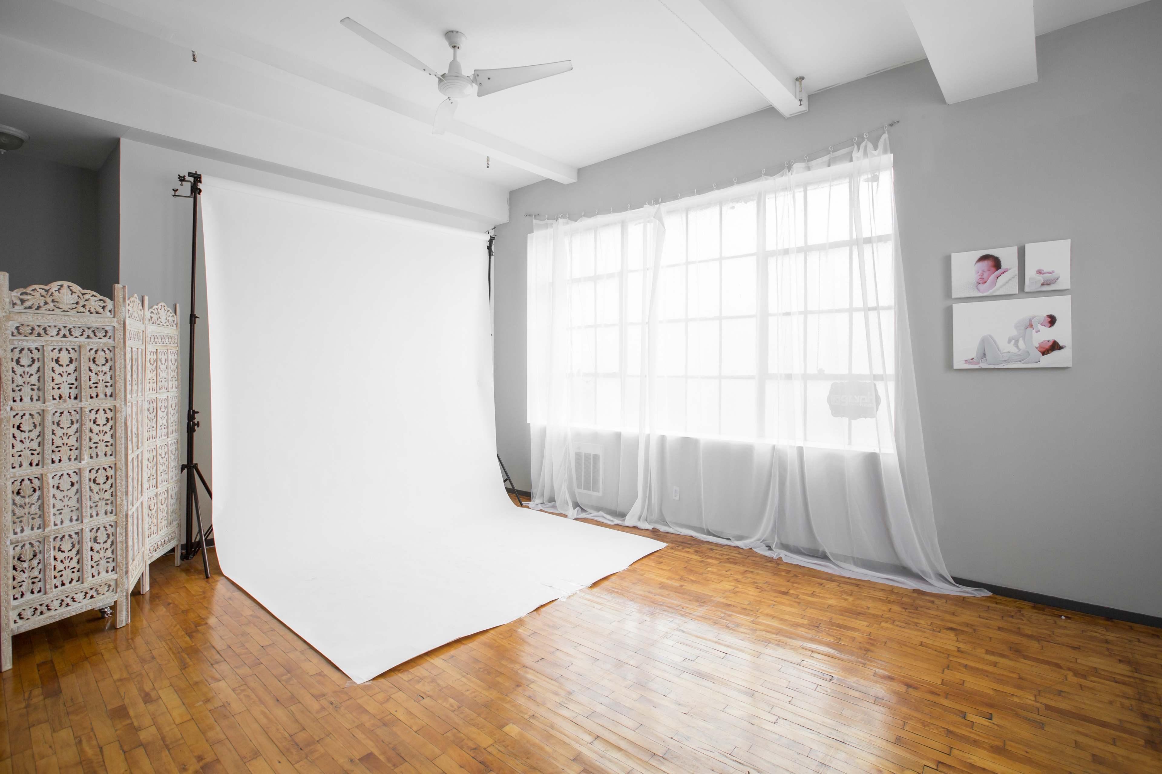 The image shows a bright, minimalistic photography studio with a white backdrop, hardwood flooring, and large windows.