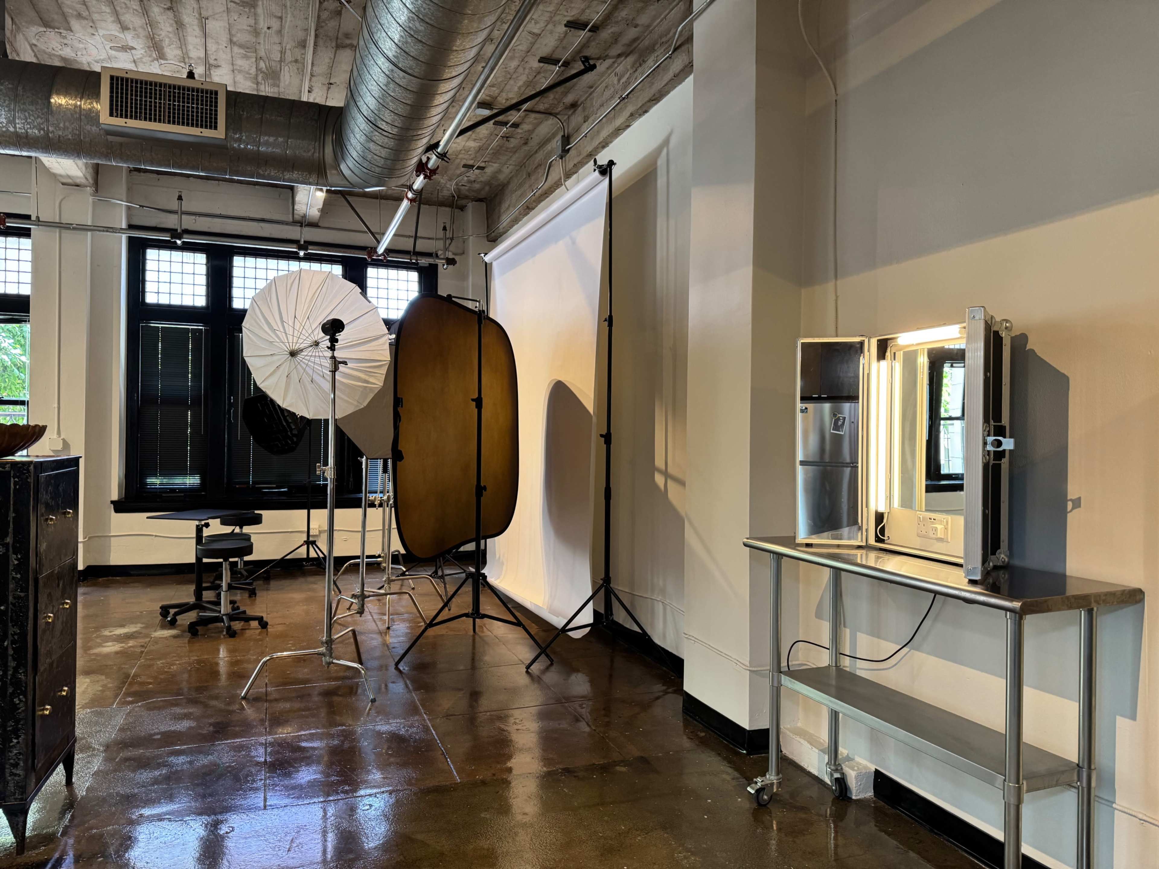 The image shows a photography studio with lighting equipment, a backdrop, a mirror, and a small table.