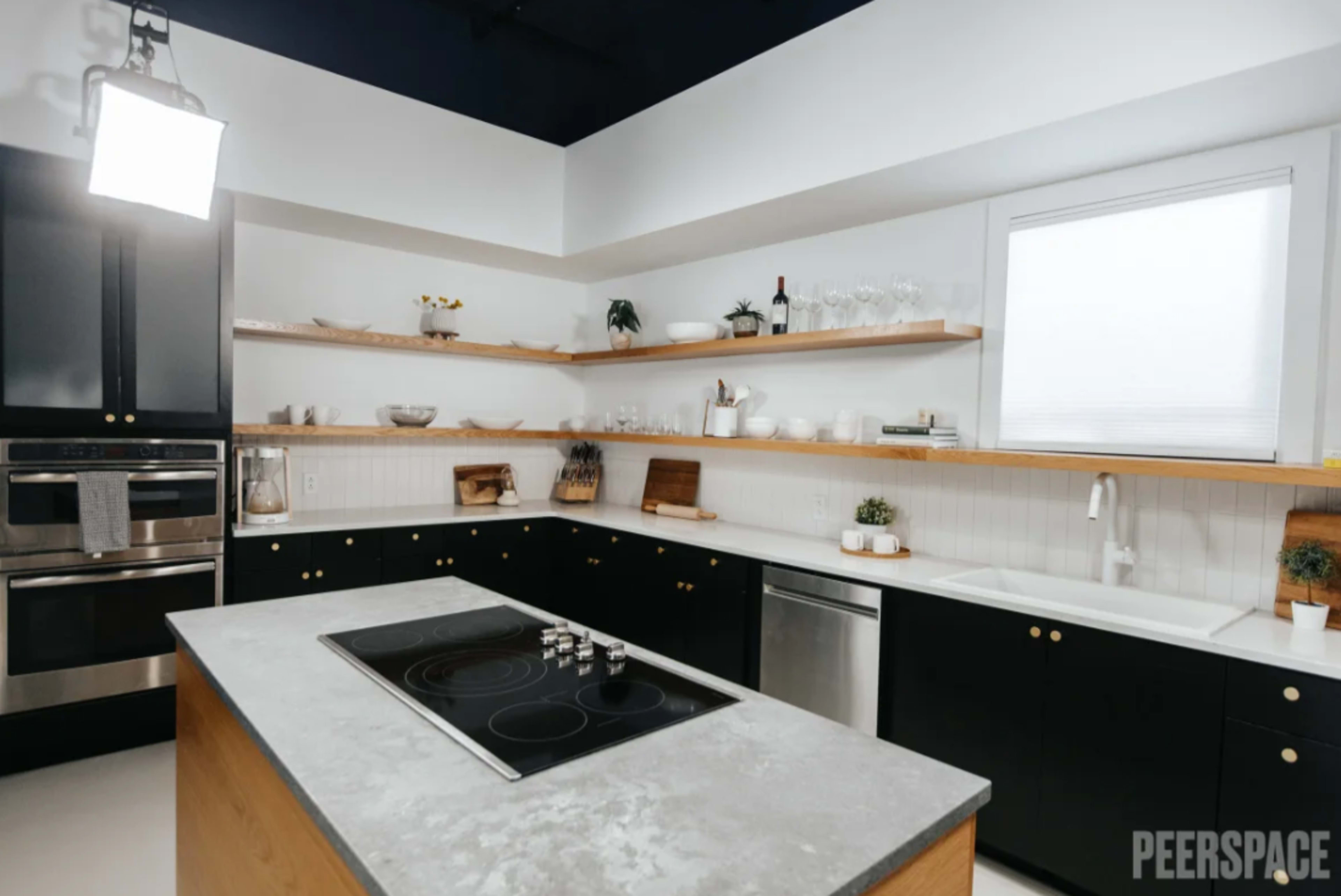 A modern kitchen with black cabinetry, wooden shelves, and a central island featuring a stovetop.