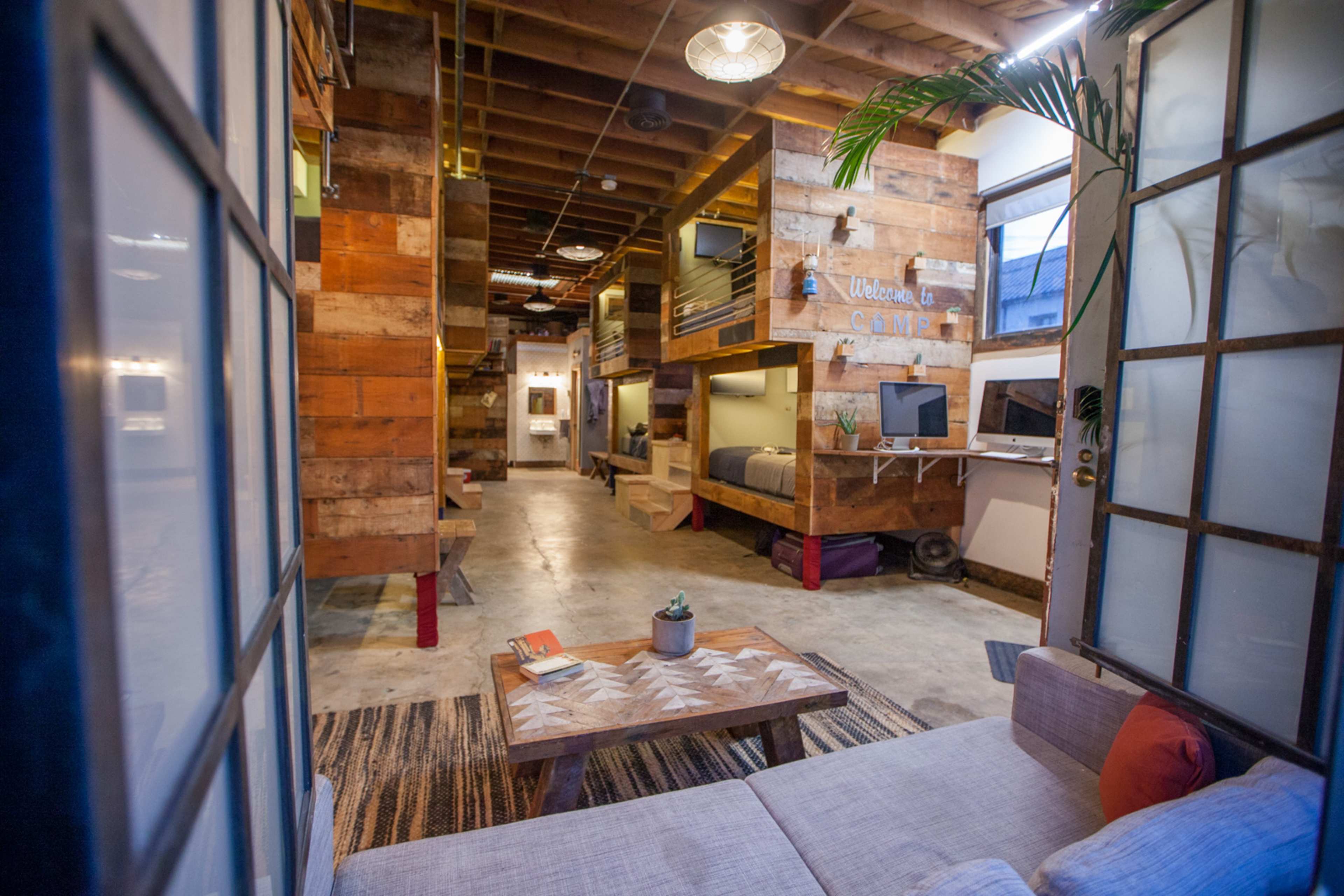 The image shows a spacious, industrial-style living area with wooden accents, multiple seating areas, and a rustic coffee table.