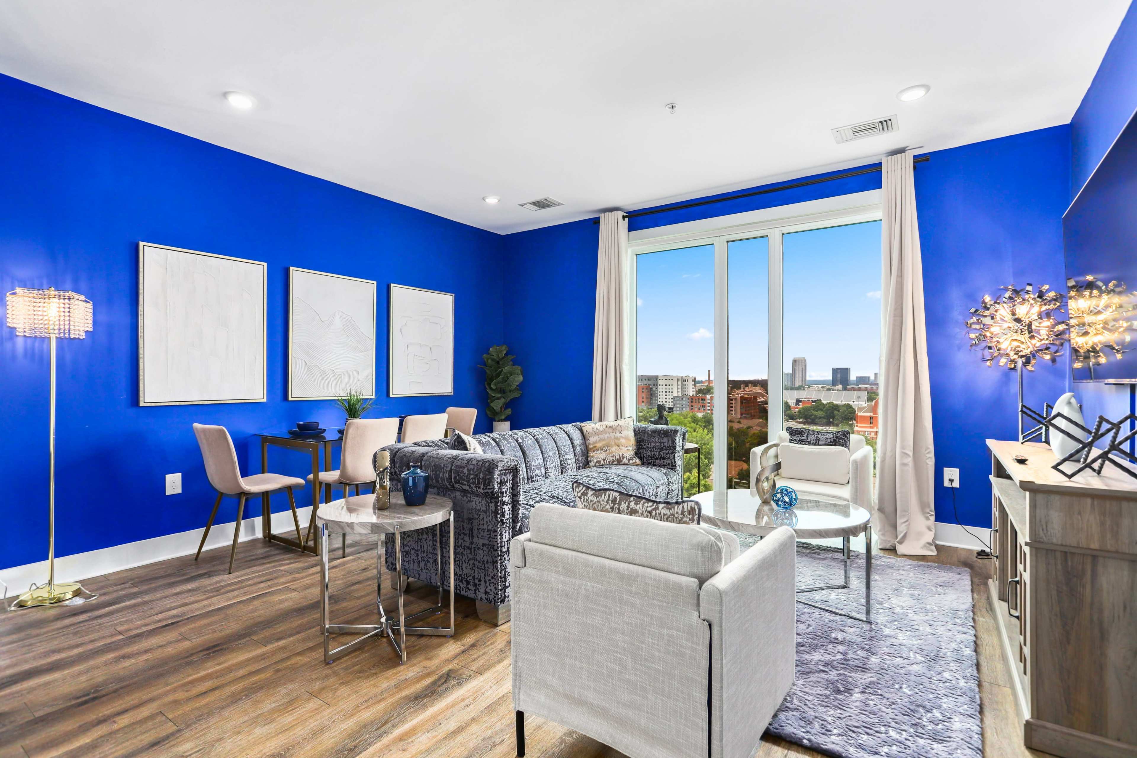 The living room features a vibrant blue accent wall, modern furniture, and large windows offering a city view.