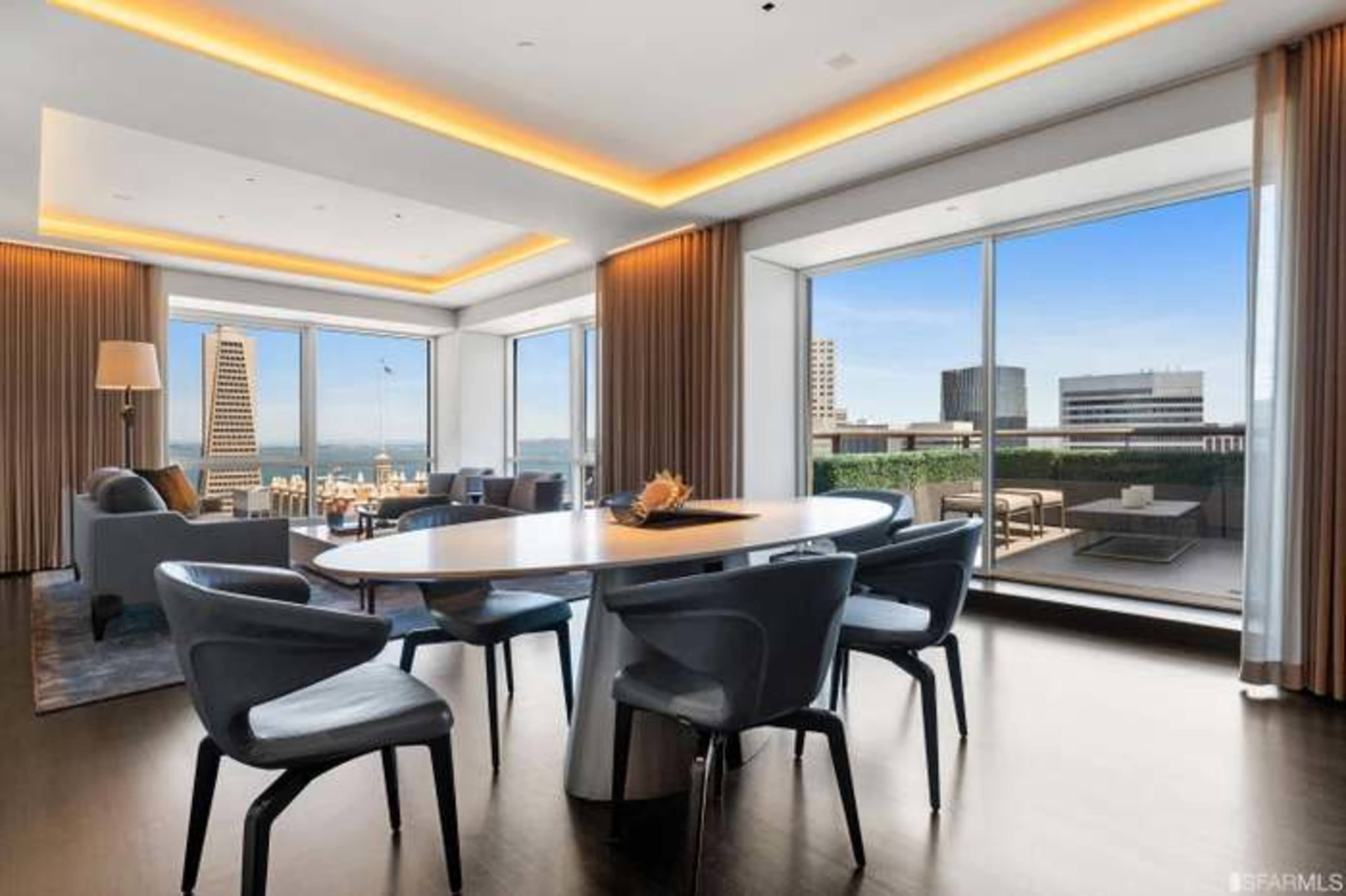 A modern living and dining area features large windows offering a view of the cityscape and a sleek table surrounded by stylish chairs.