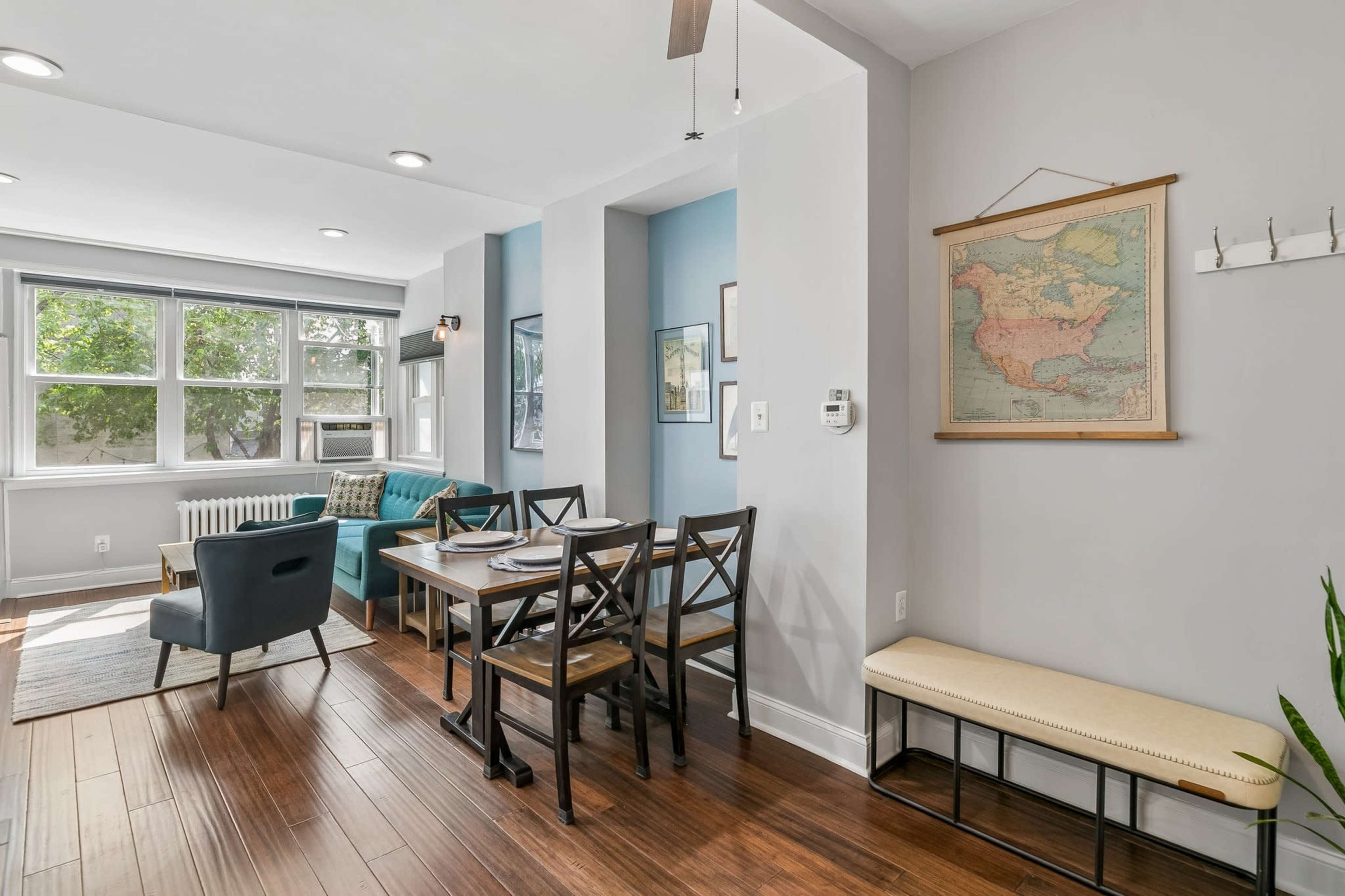 The image shows a modern dining area with a table and chairs, adjacent to a living space featuring a blue sofa and a wall with a map.