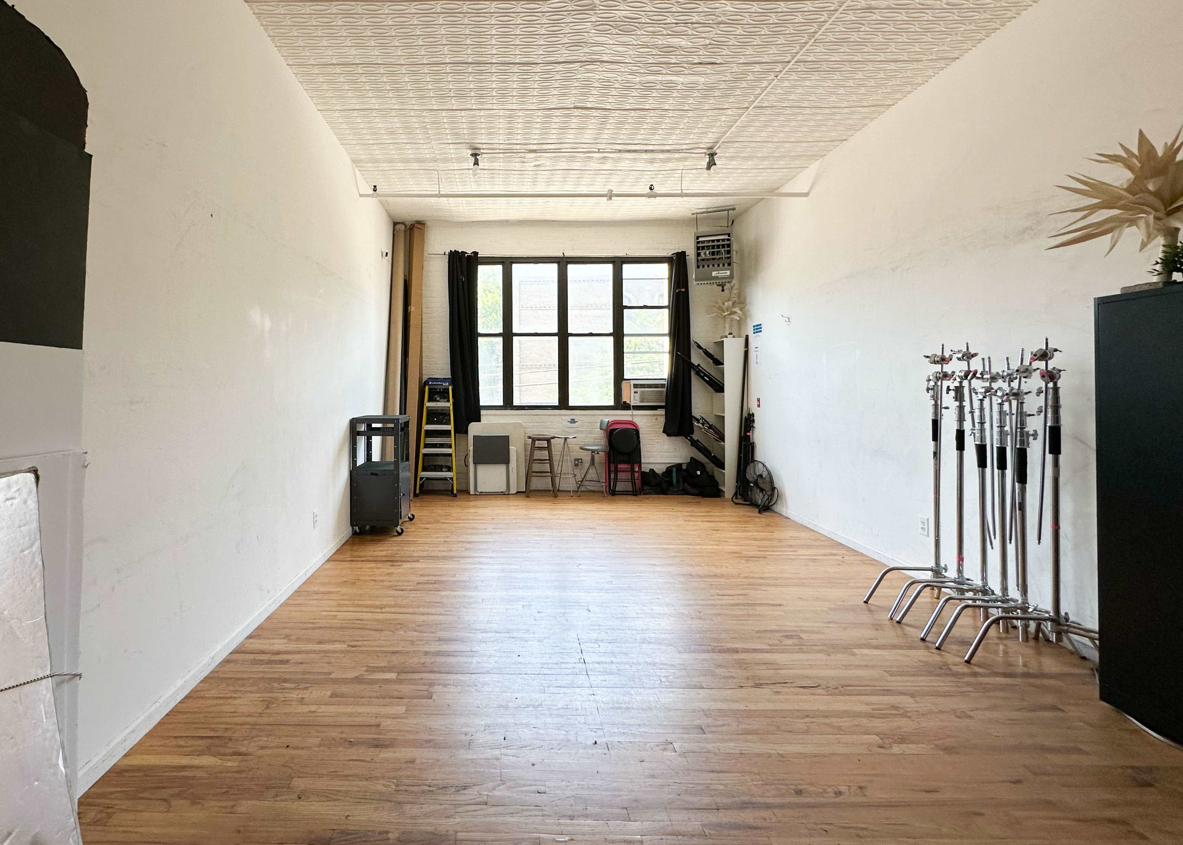 An empty interior space with wooden flooring, large windows, and minimal furnishings along the walls.