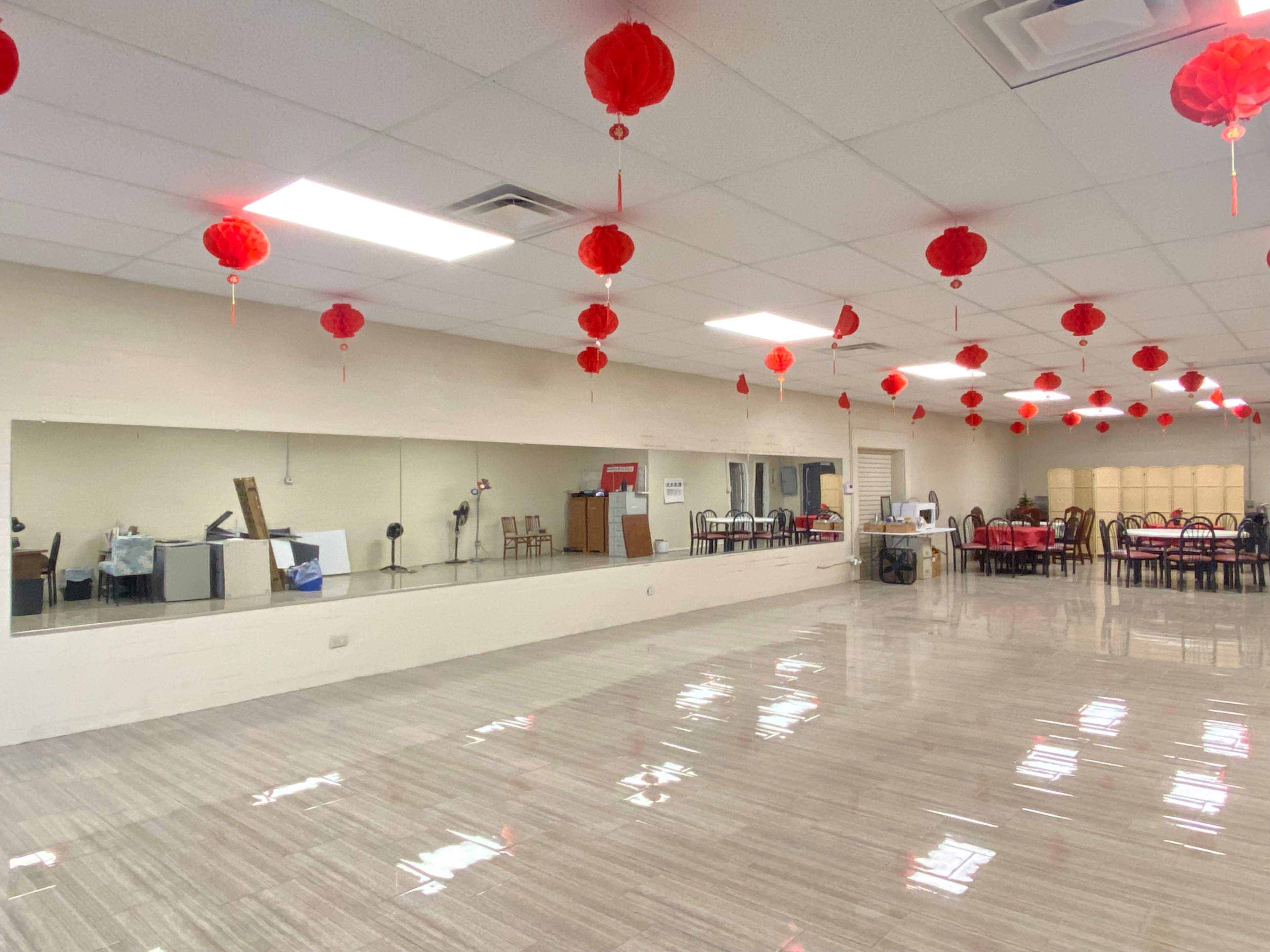 A spacious room with a mirrored wall, red lanterns hanging from the ceiling, and tables arranged for dining.