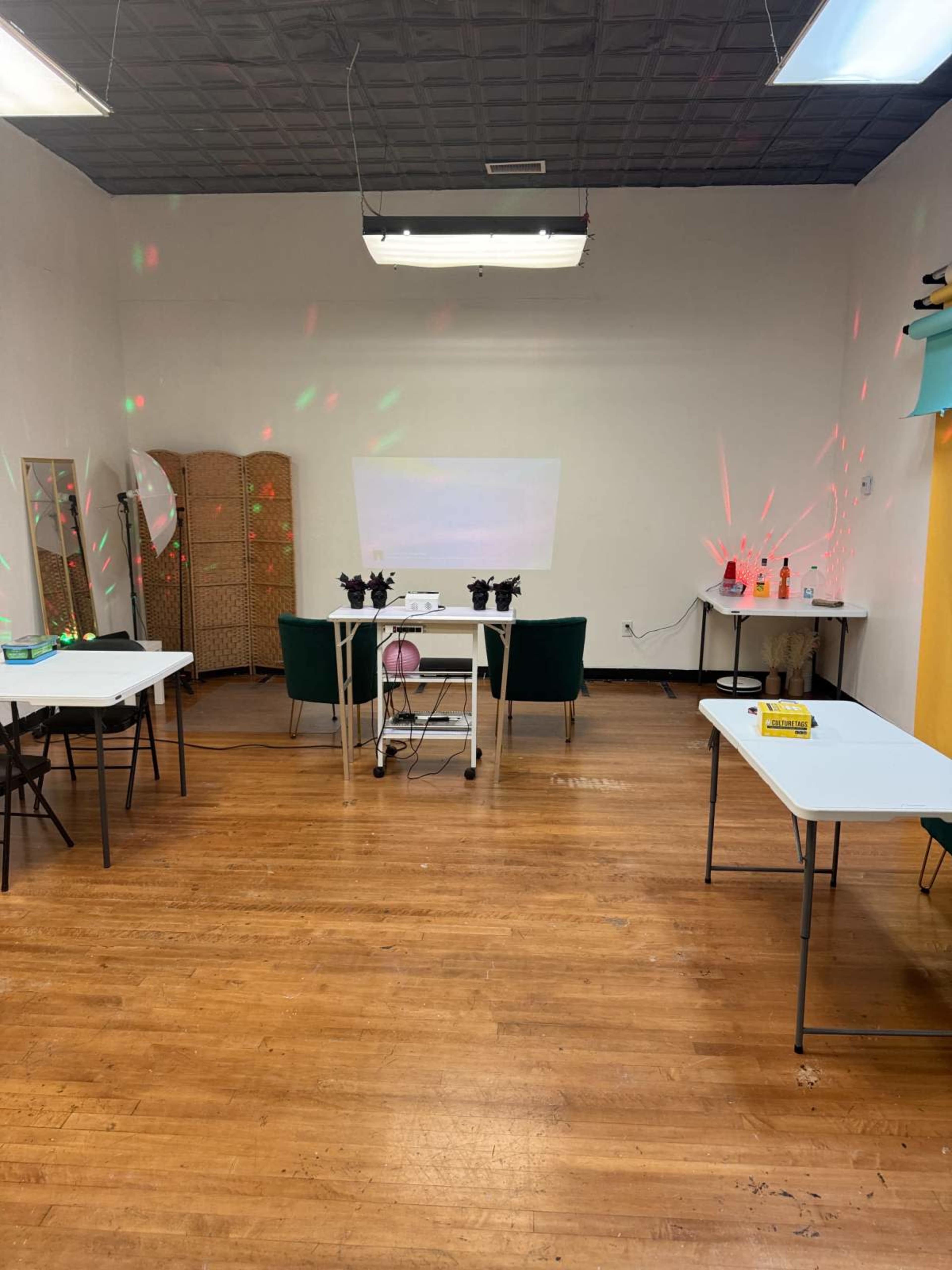 The image shows a spacious room with tables arranged in a U-shape, a projector screen, and some decorative lights along the walls.