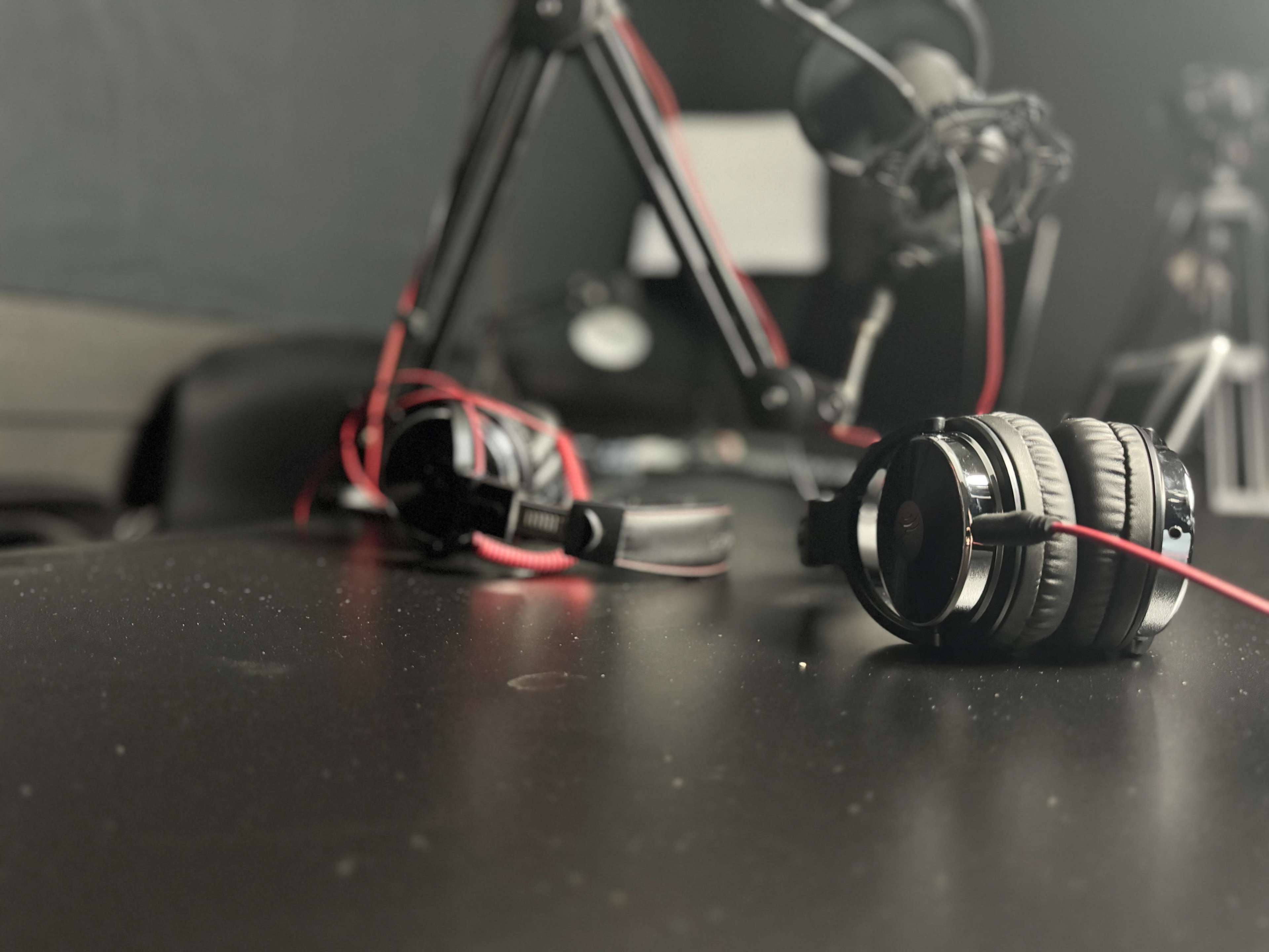 The image shows a black table with headphones and a microphone setup in a studio environment.