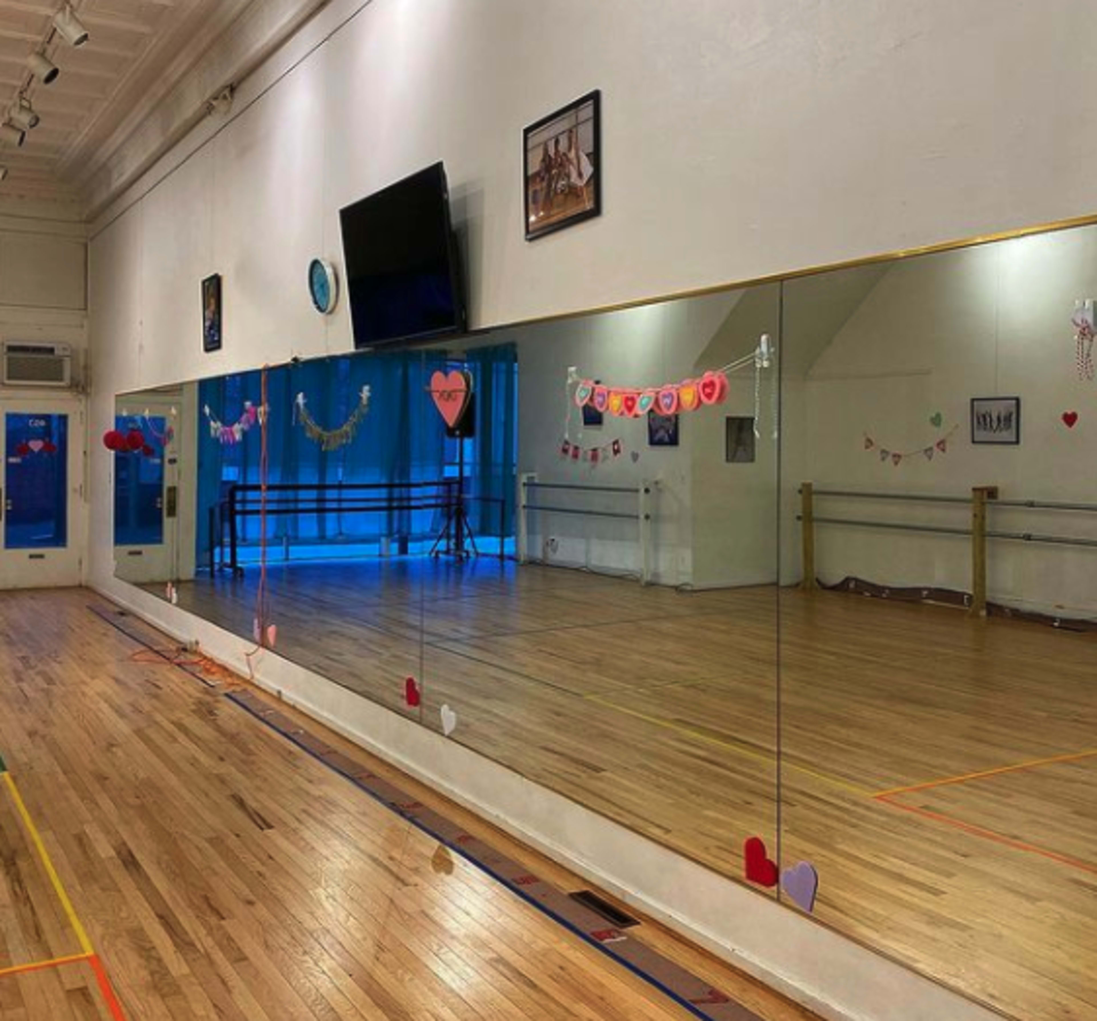 A dance studio with wooden flooring, large mirrors along one wall, and decorations including hearts and banners.