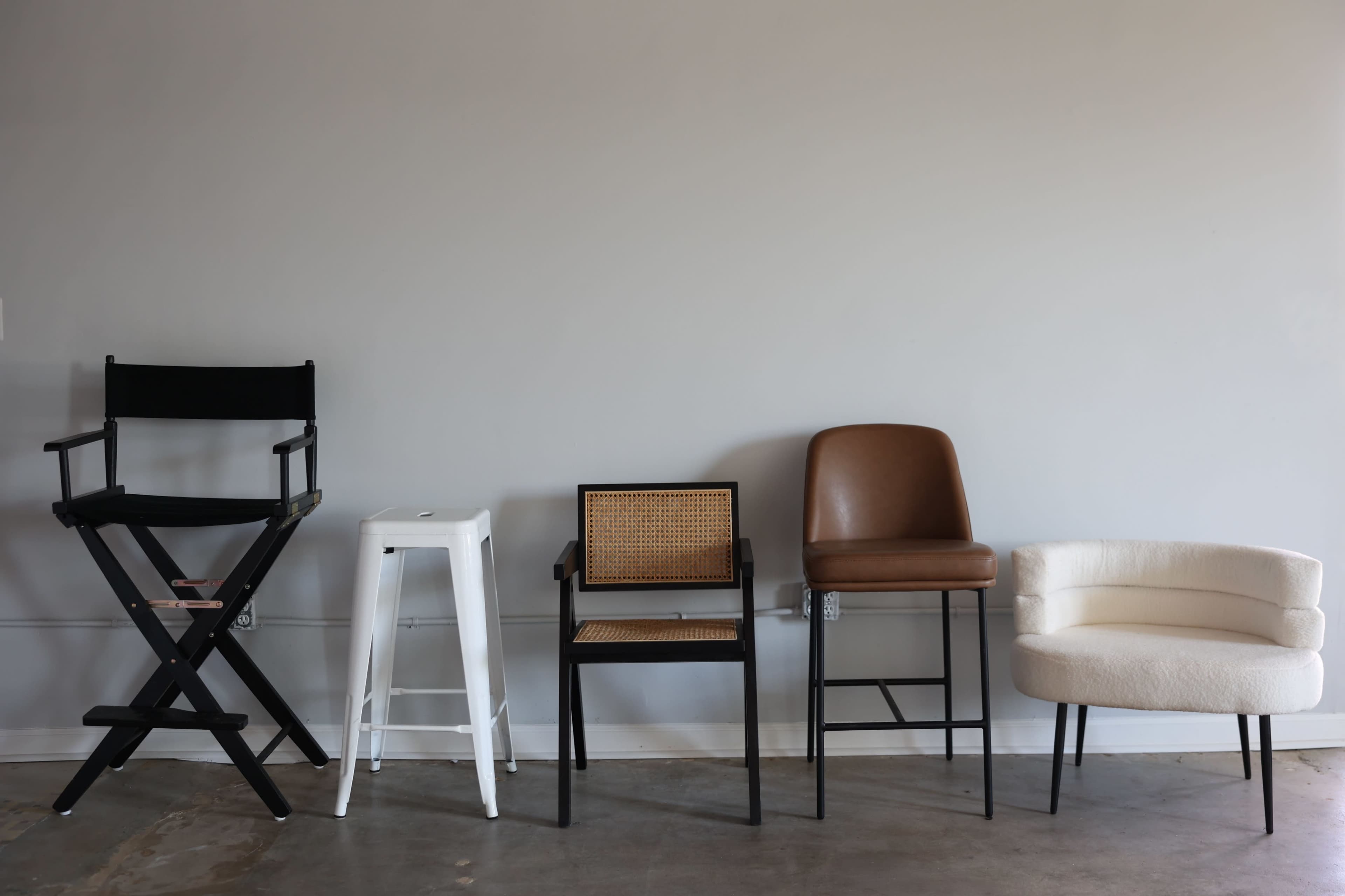Five different styles of chairs are lined up against a gray wall, showcasing a variety of materials and designs.