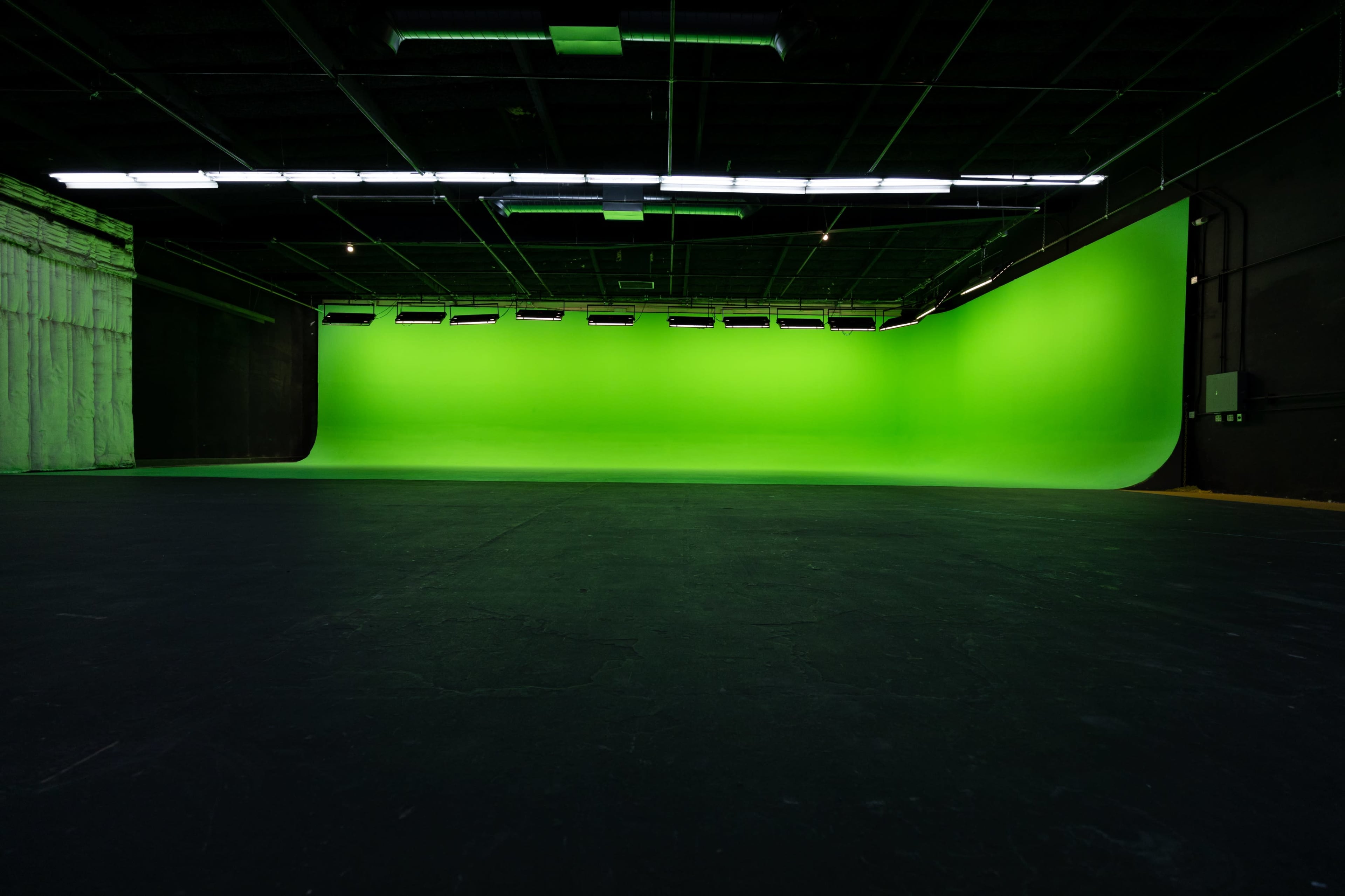 The image shows a large, empty studio space with a bright green backdrop and a dark floor.