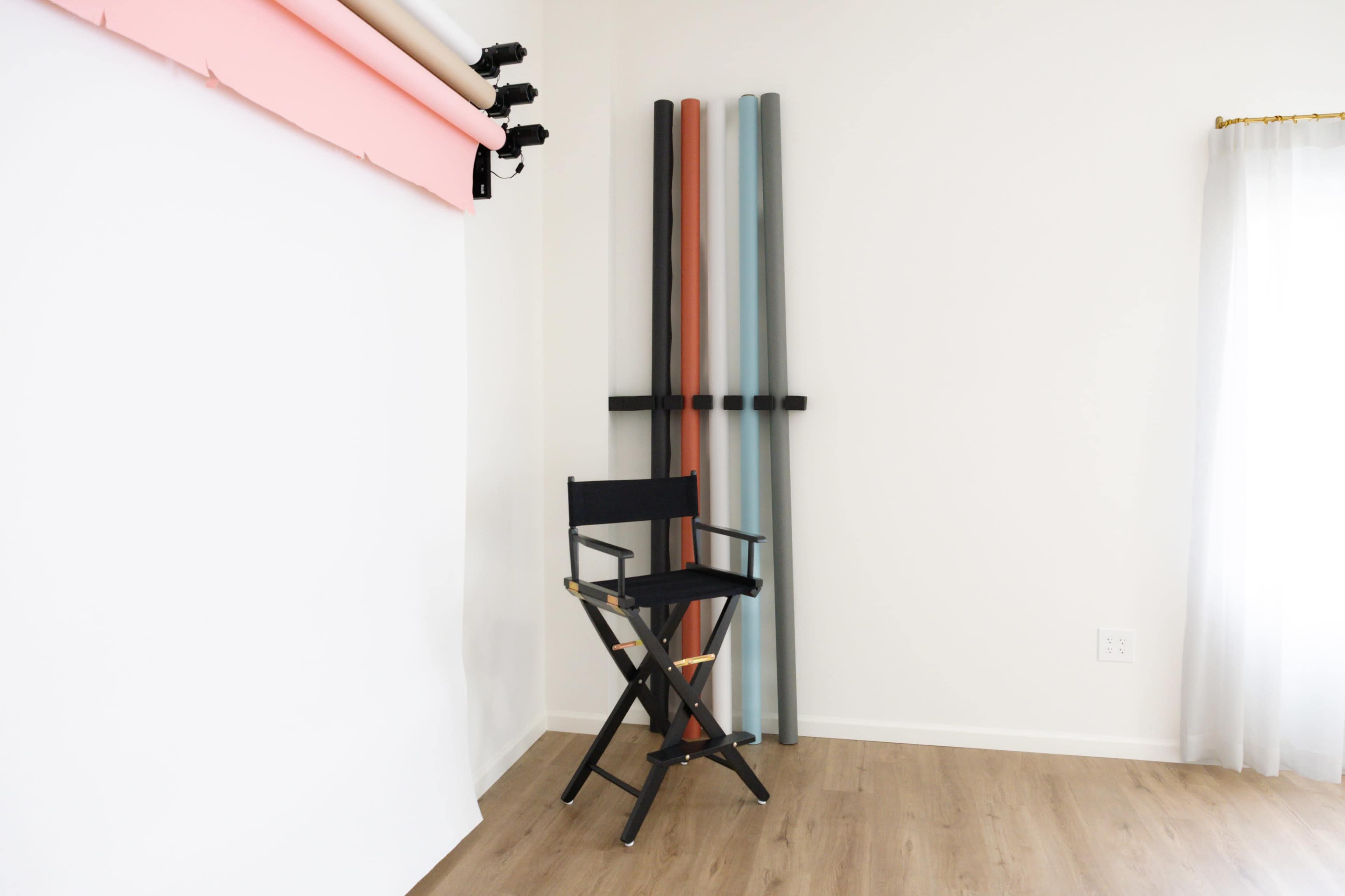 A black director's chair is positioned next to several rolls of backdrop paper in a well-lit studio space.