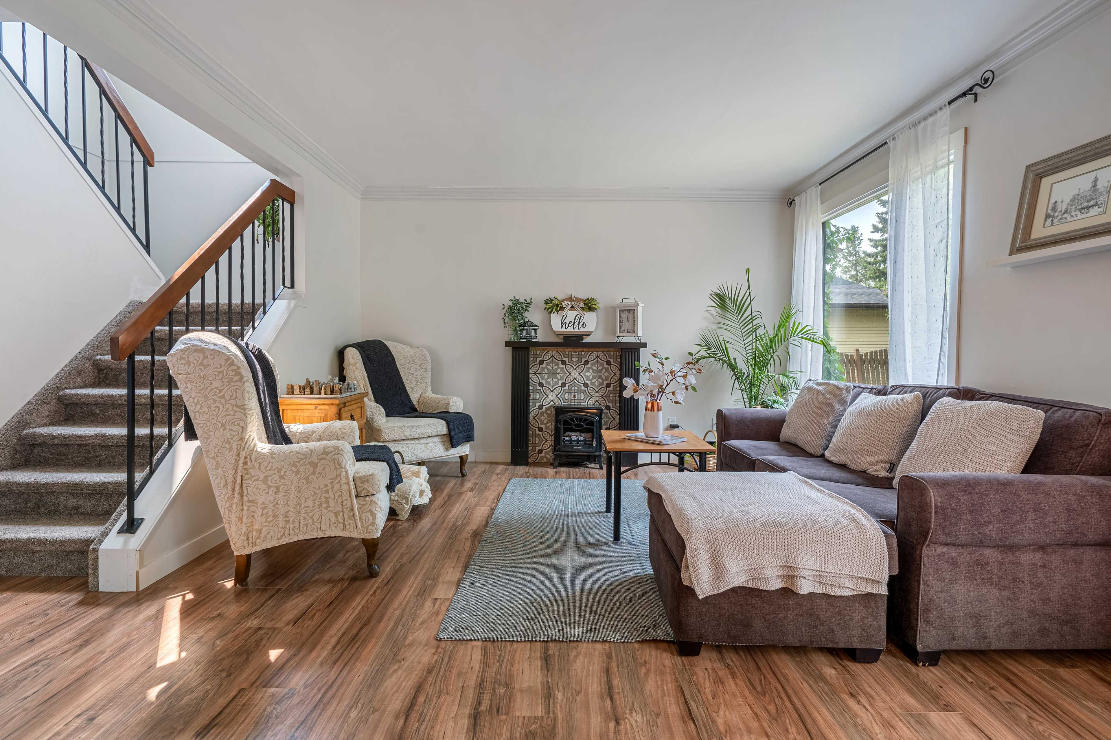 A living room with a staircase, featuring two armchairs, a brown sofa, a coffee table, and a decorative fireplace.