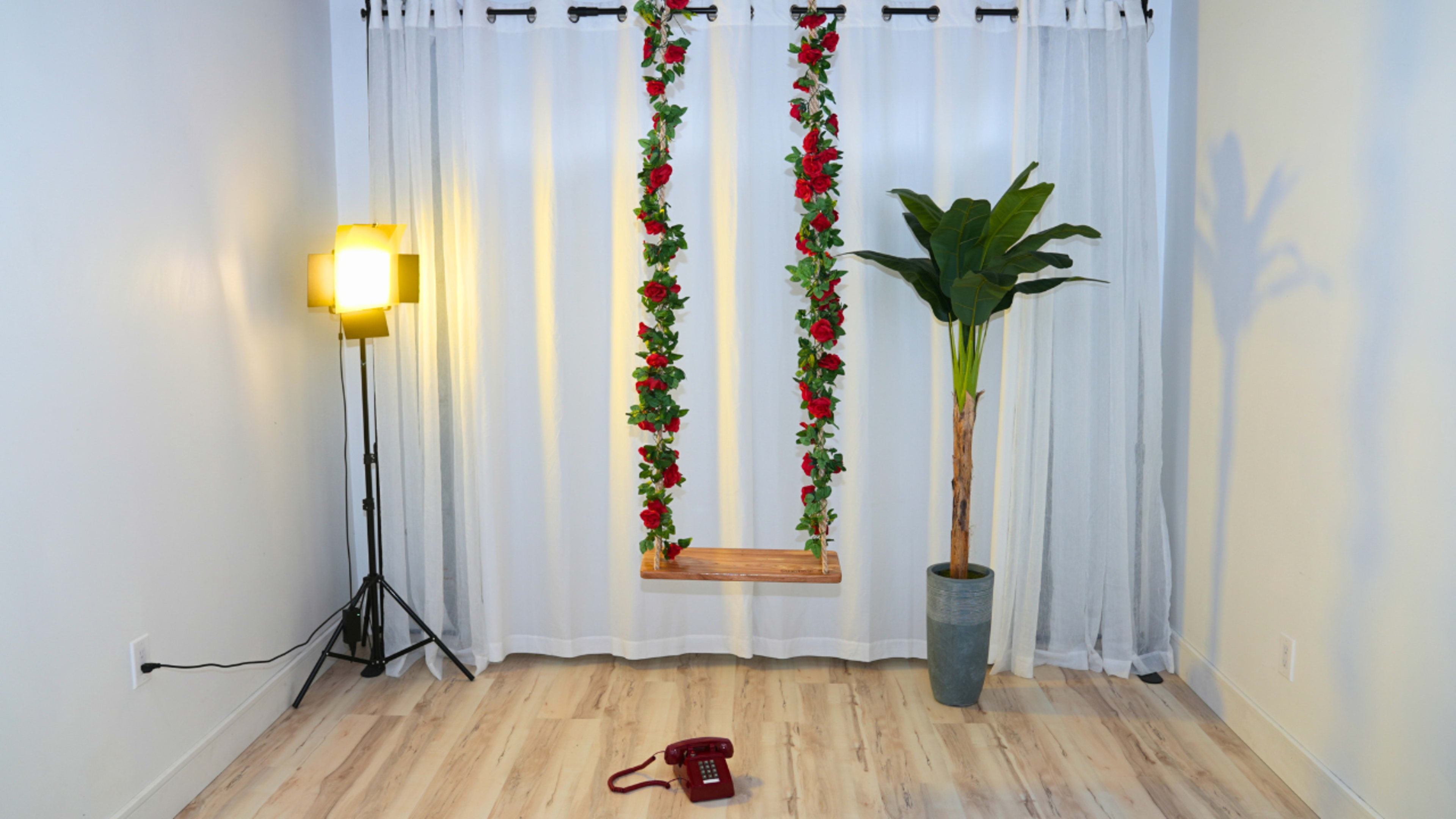 The image shows a bright room with a swing adorned with flowers, a potted plant in the corner, and an old-fashioned red telephone on the floor.