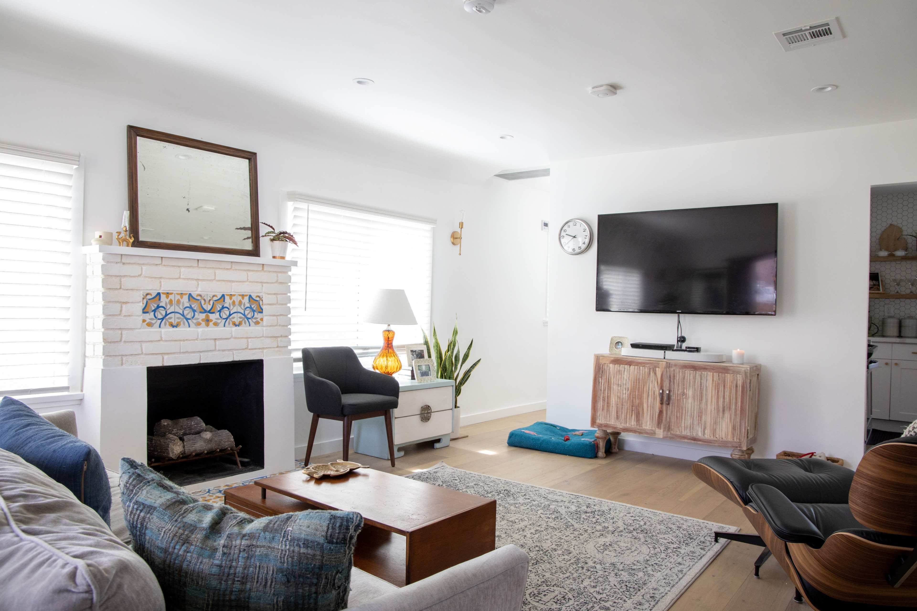 A bright living room features a white brick fireplace, a mounted television, a wooden console, and modern seating arrangements.