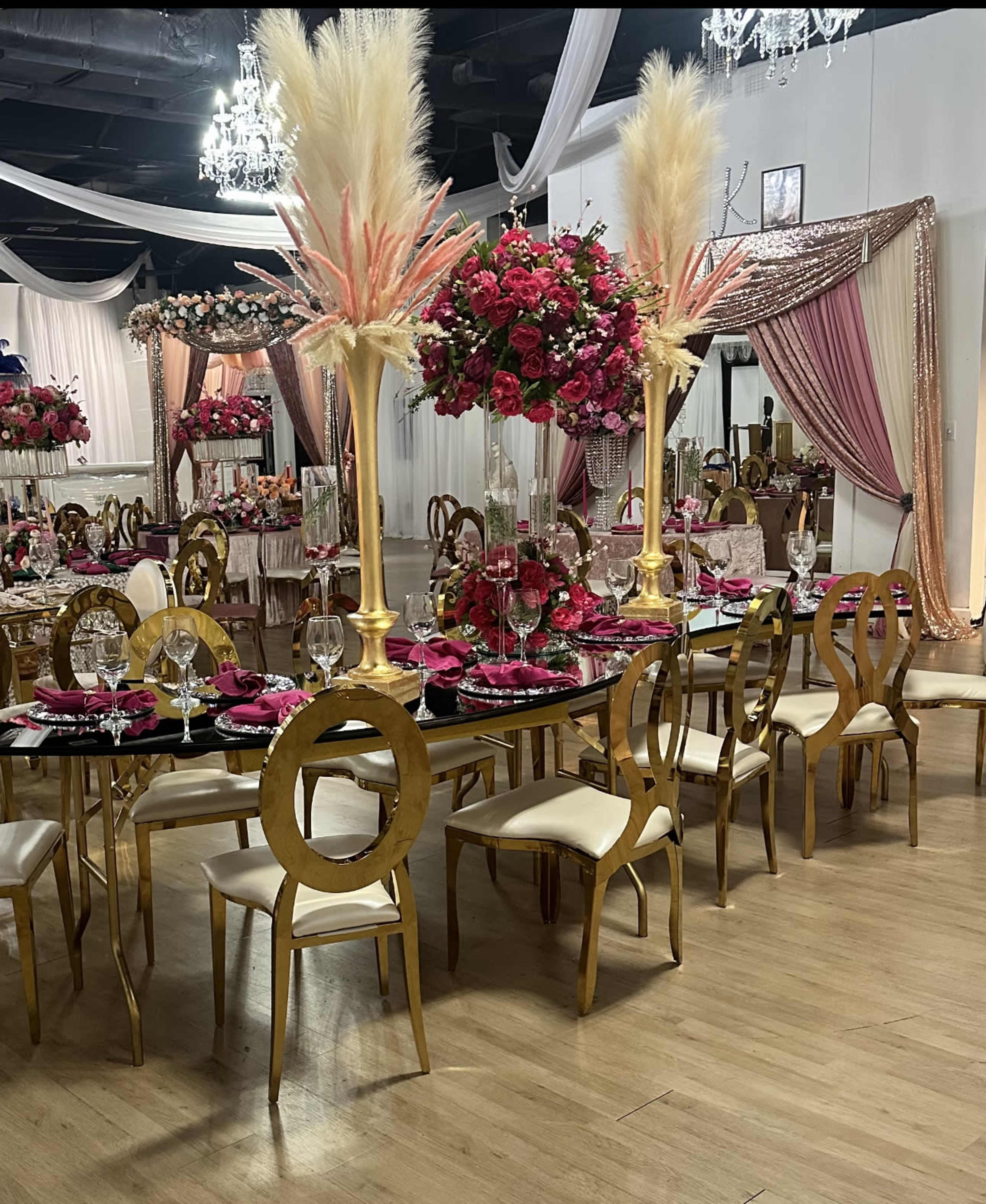 An elegantly decorated banquet hall with gold-accented tables set for a feast, featuring tall floral centerpieces and pink table settings.