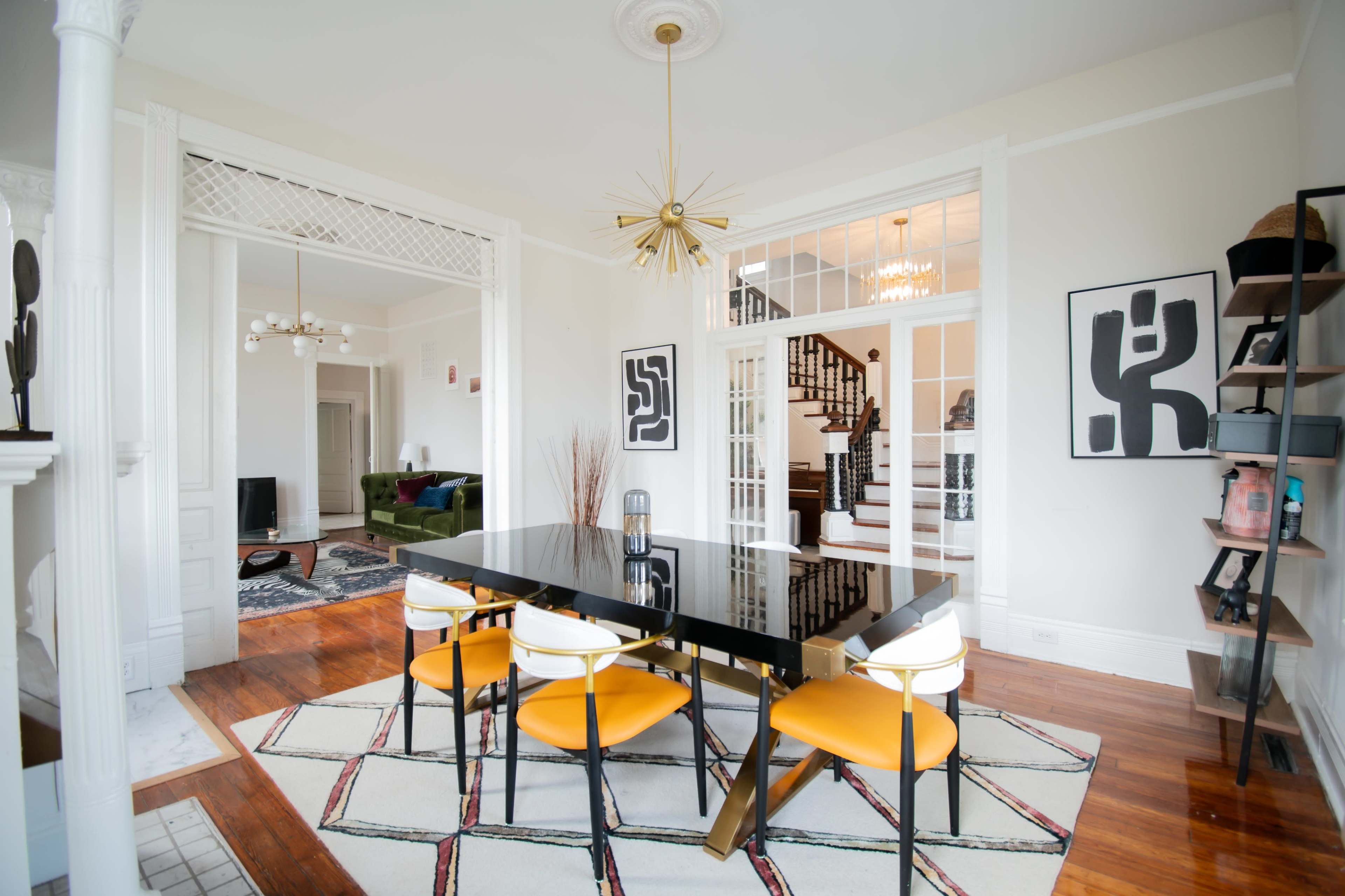 A modern dining area features a black table with yellow chairs, surrounded by artwork and an open view of a staircase.