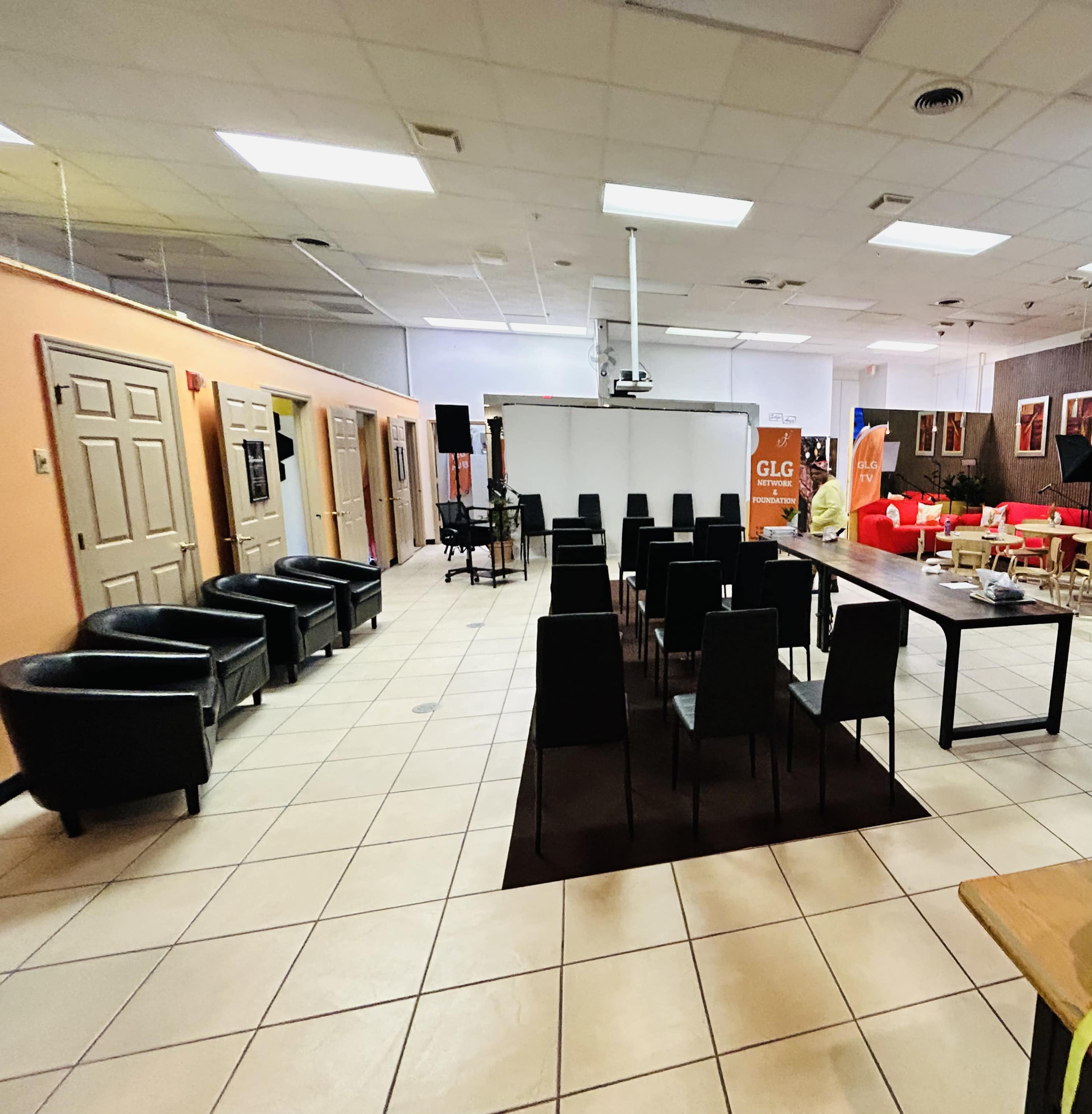 A spacious, sparsely furnished room with black chairs arranged around a table, and various doors leading to other areas.