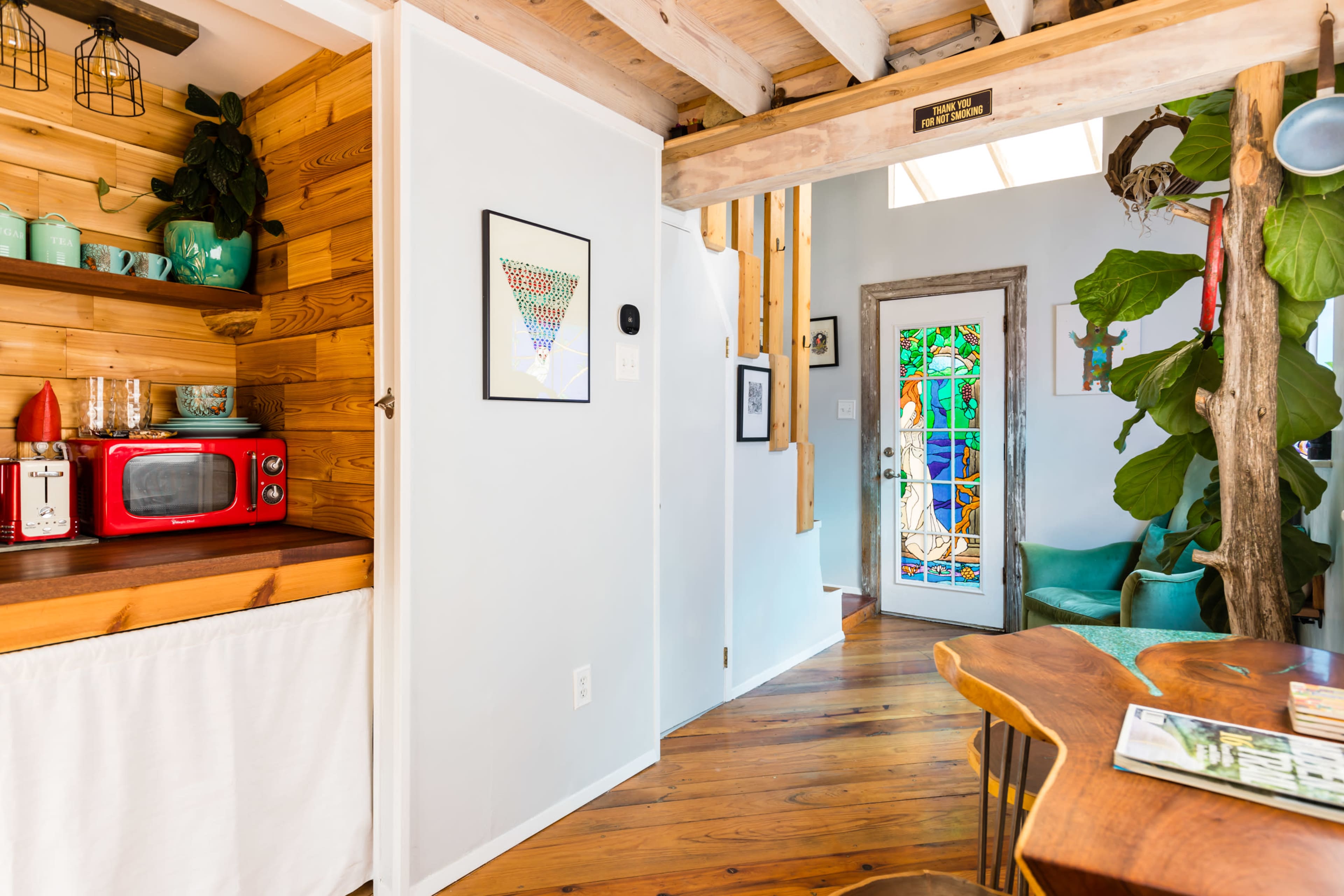 A bright interior space featuring a kitchen area with a red microwave, a dining table, and a stained glass door leading outside.