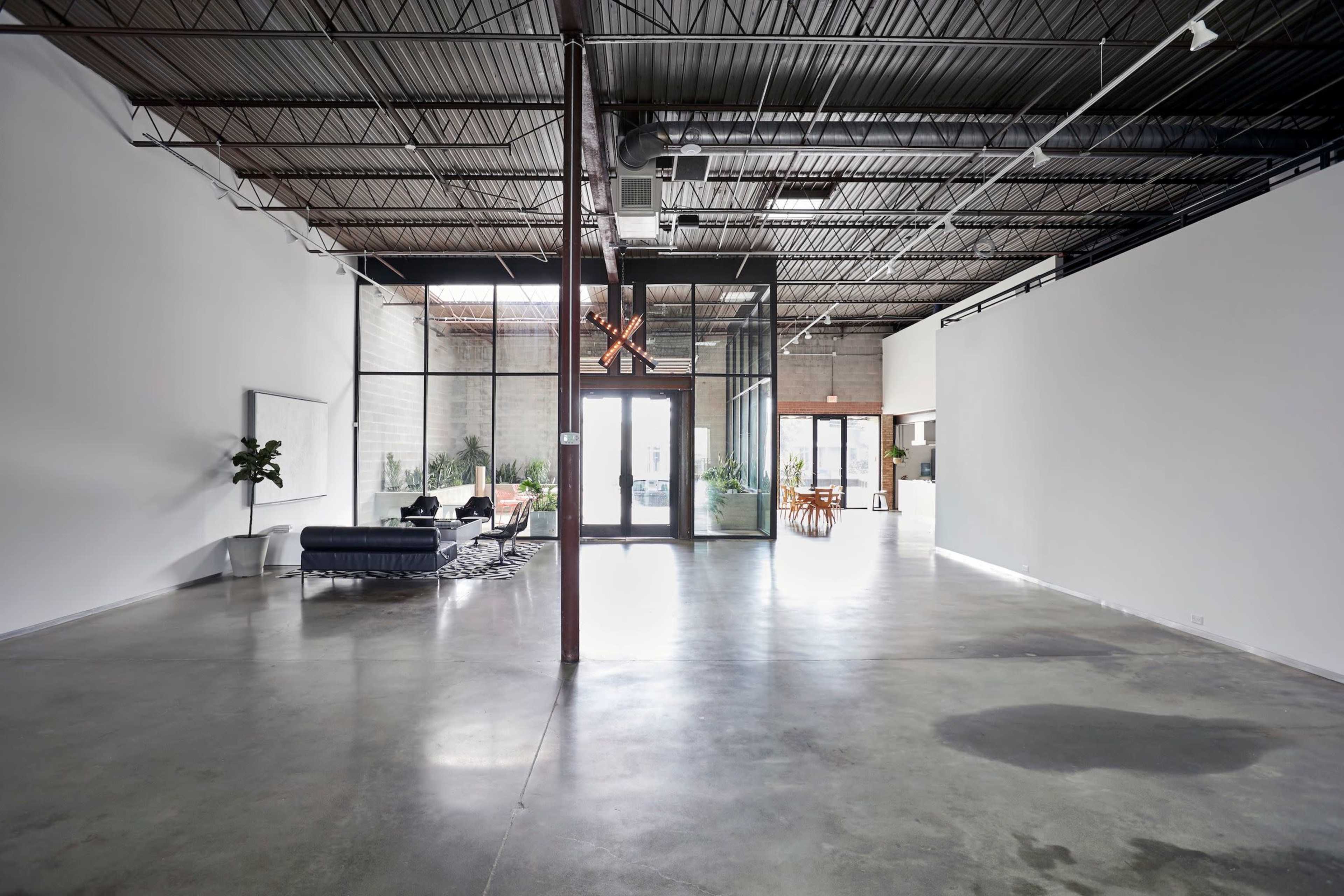 An open, spacious interior with polished concrete flooring, large glass doors, and minimal furnishings.