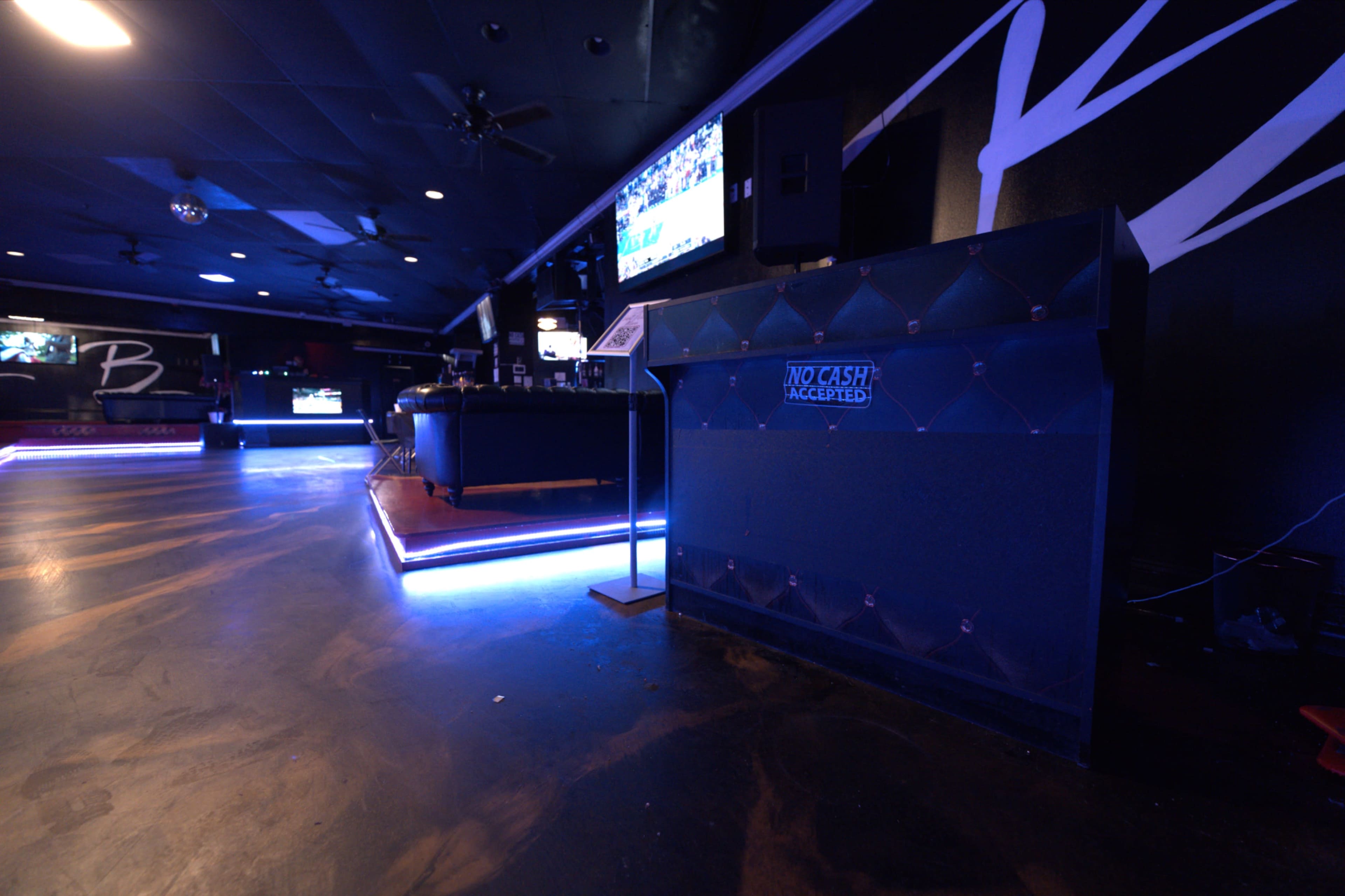 The image shows a dimly lit lounge area with a blue illuminated counter and a television on the wall.