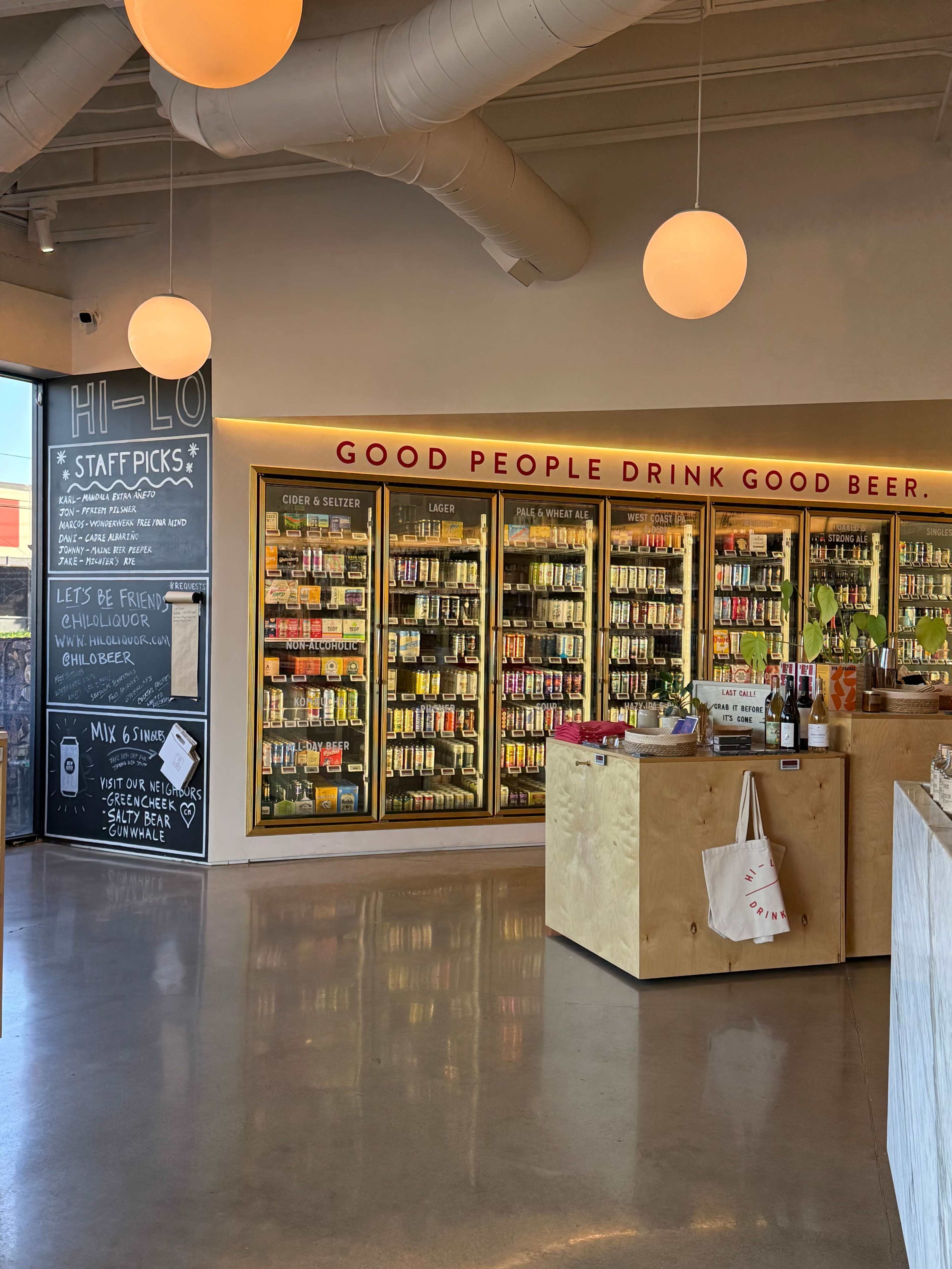 The image shows an interior of a beverage store featuring shelves stocked with various canned and bottled drinks, illuminated by pendant lights.