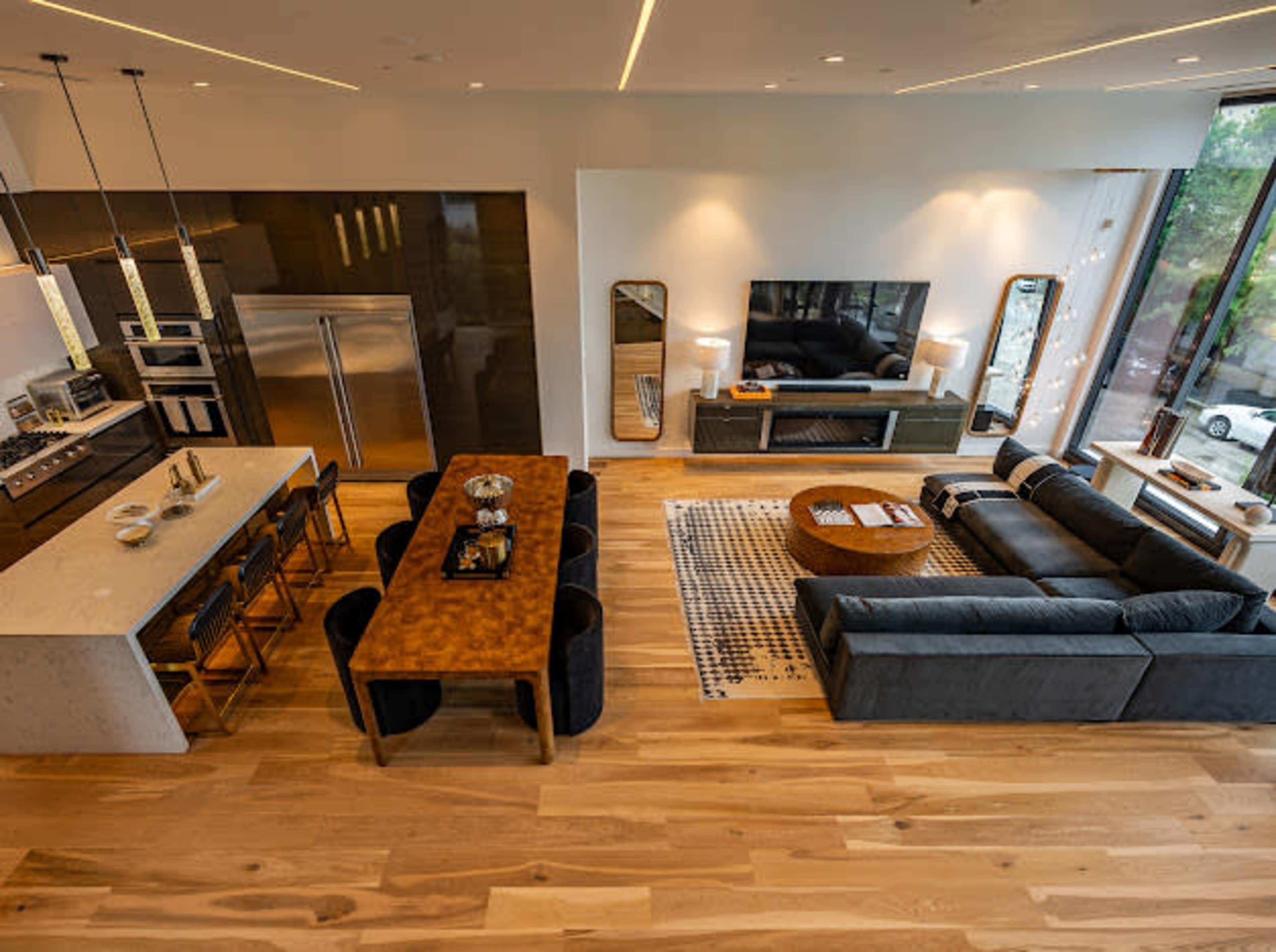 The image shows a modern living space featuring a kitchen with a dining area and a seating area arranged around a television.