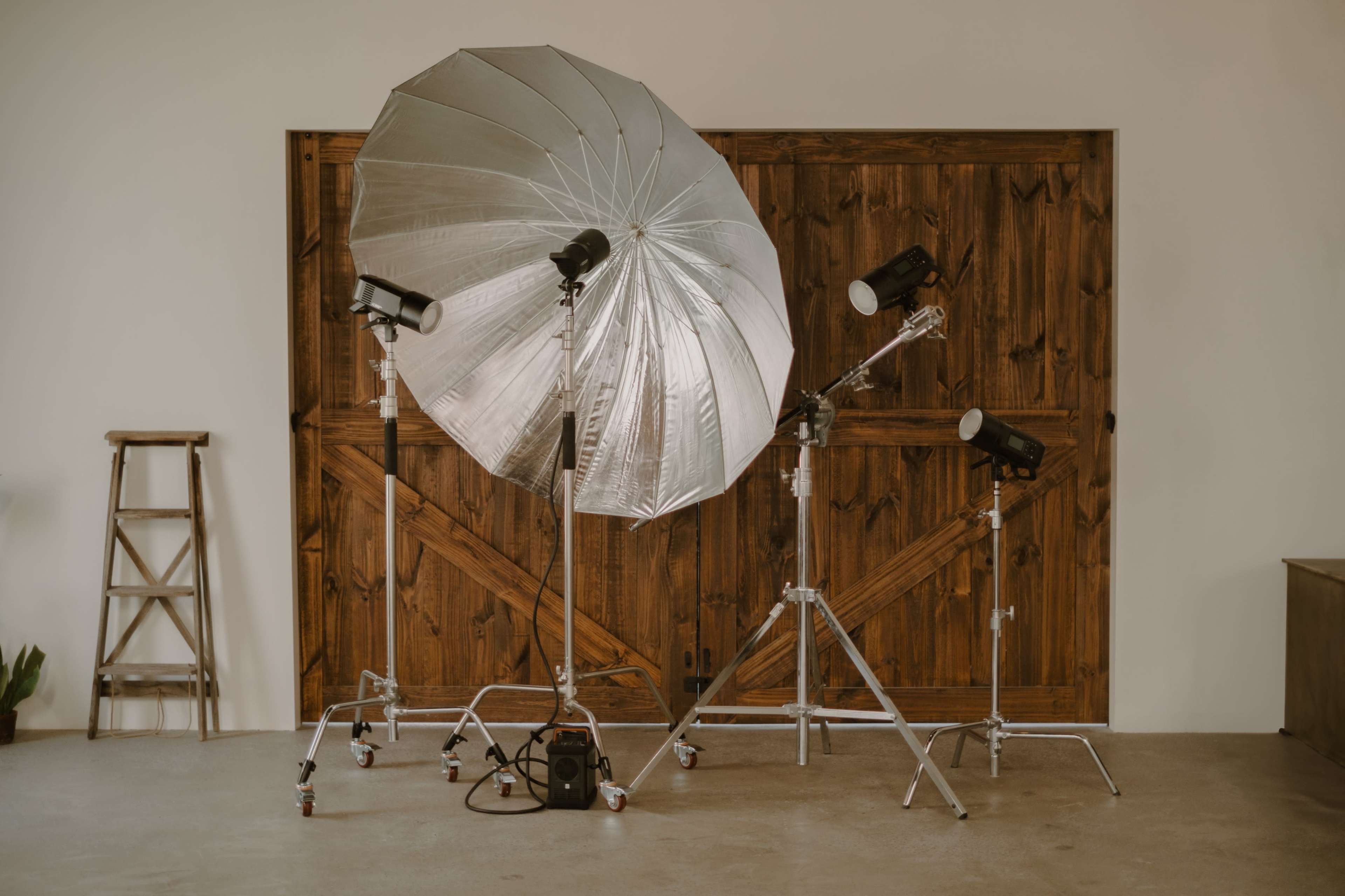 A photography studio setup featuring a large umbrella reflector and several lighting equipment on stands in front of a wooden backdrop.