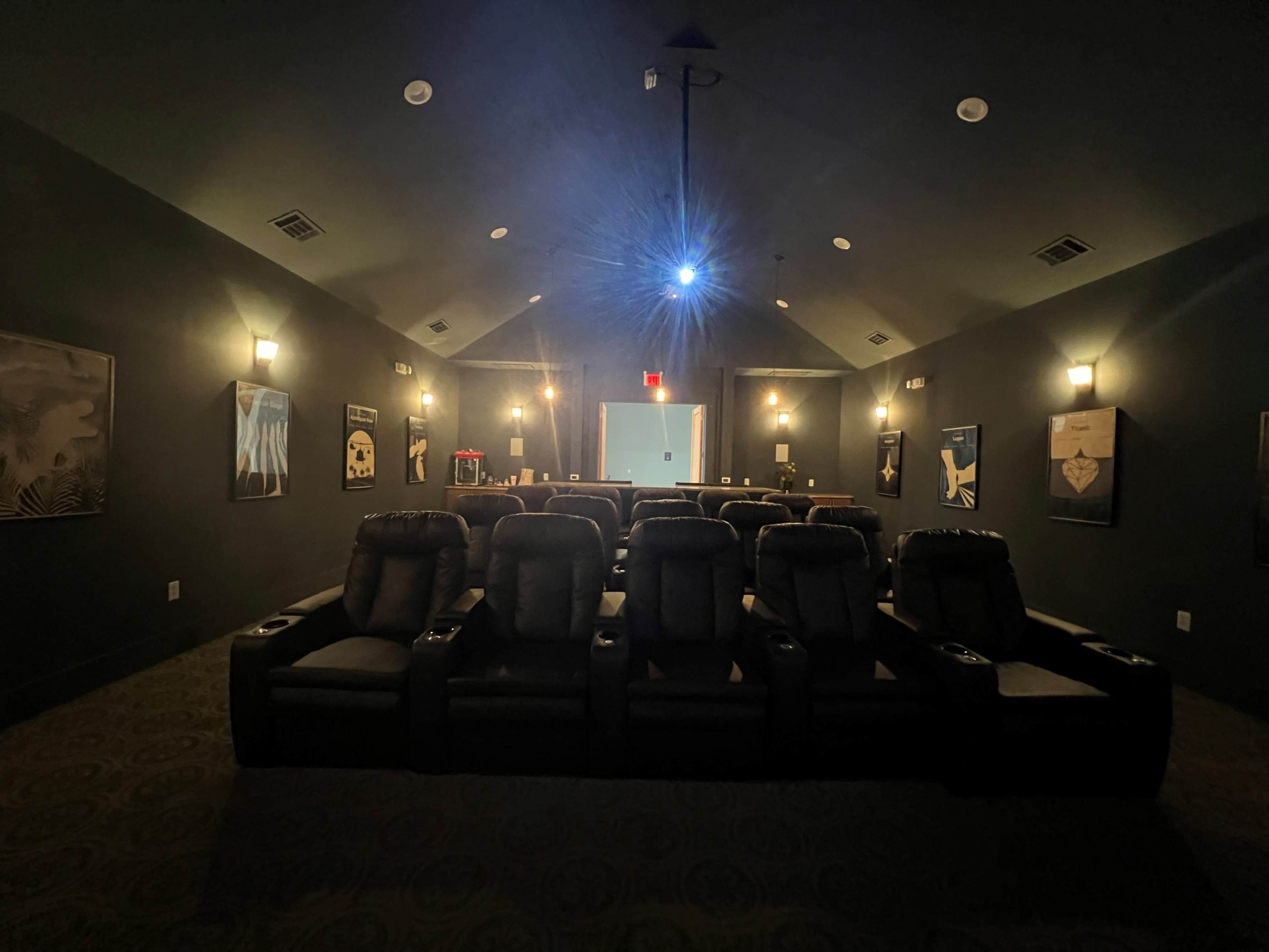 A dimly lit home theater with black reclining chairs arranged in rows facing a screen at the front.