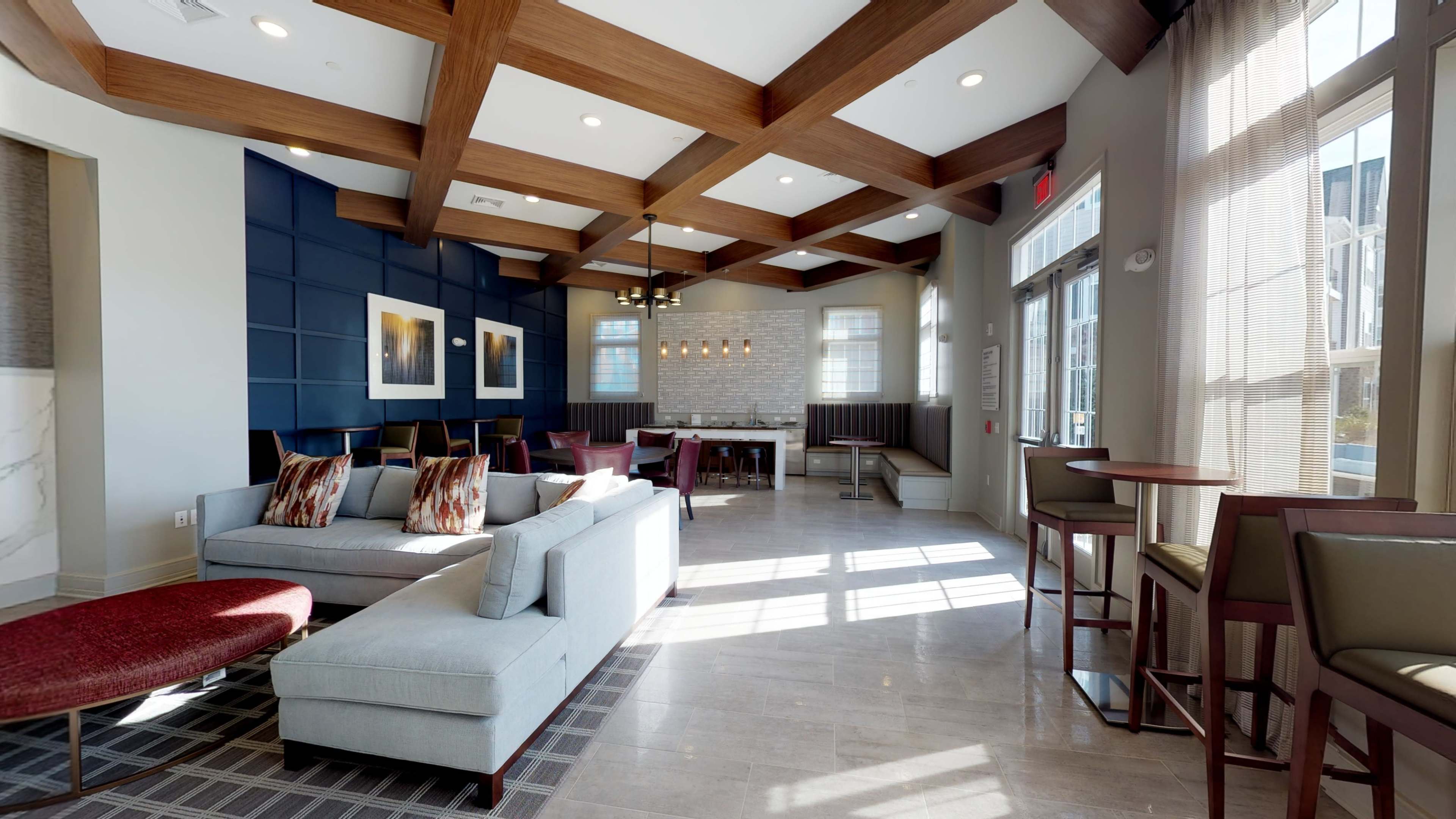 A modern lounge area features a sectional sofa, wooden beams on the ceiling, and a dining area with a large table and chairs.