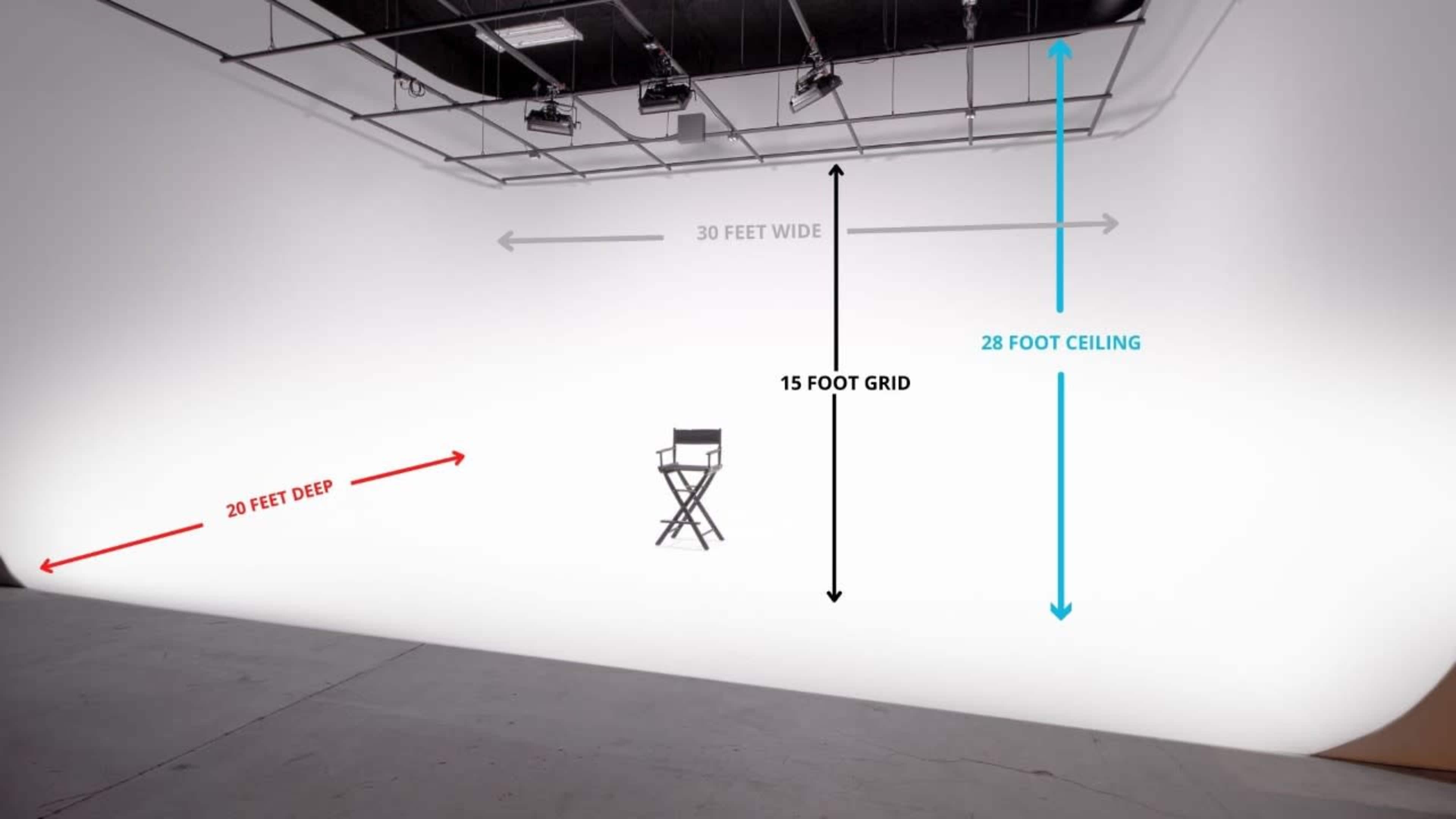 A spacious studio setup featuring a 30-foot wide and 20-foot deep area with a 28-foot ceiling, highlighted by grid lines and a director's chair in the center.