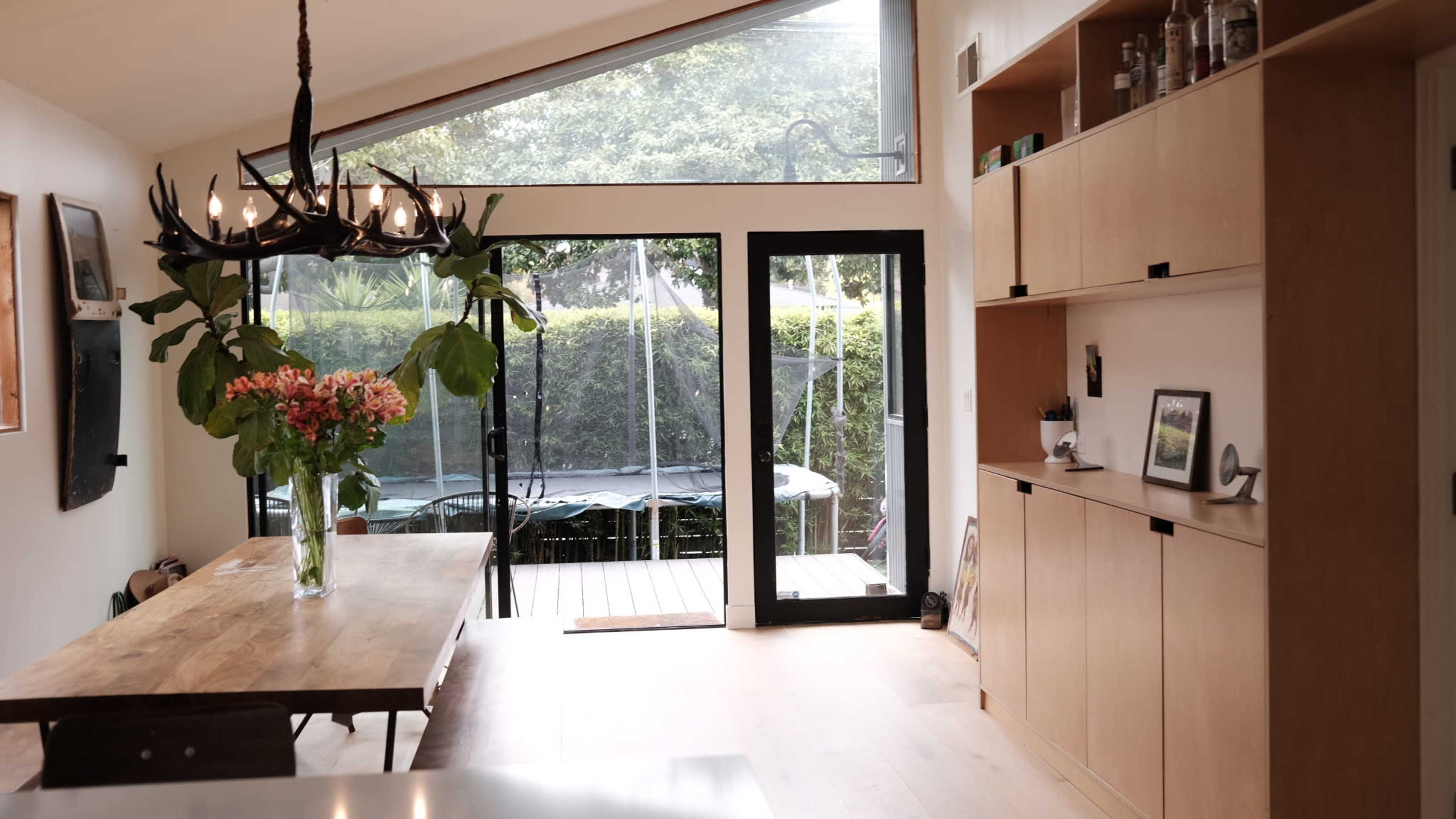 A dining area features a wooden table, large windows letting in natural light, and a door leading to a patio with a trampoline.