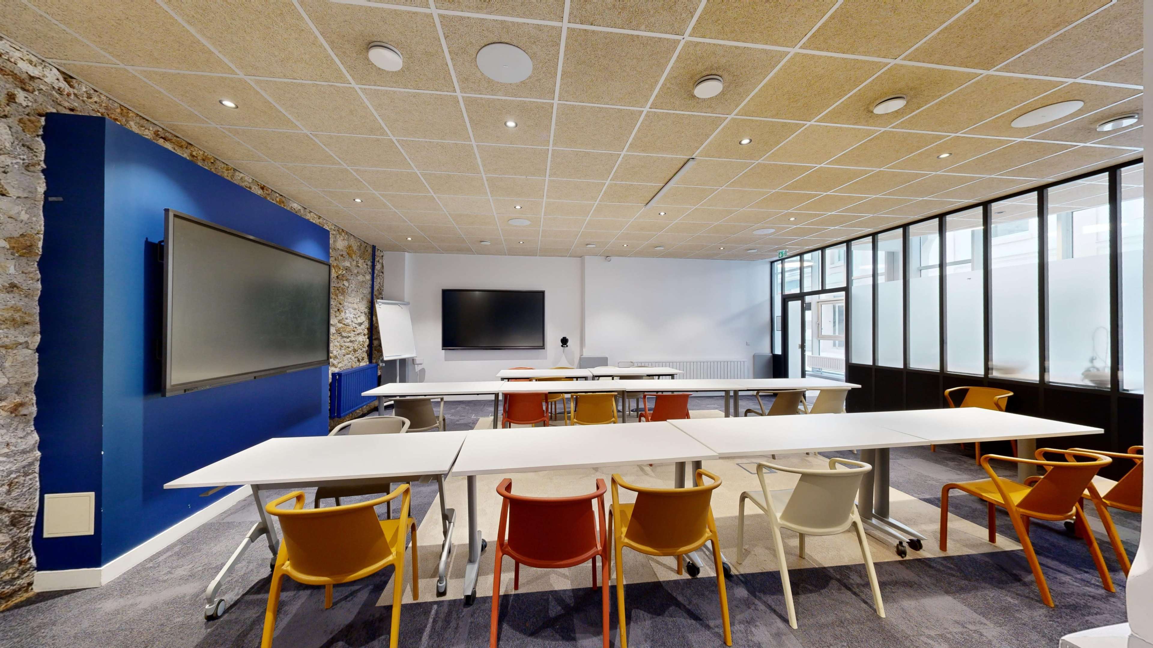 A modern conference room features multiple tables, colorful chairs, and large screens for presentations.