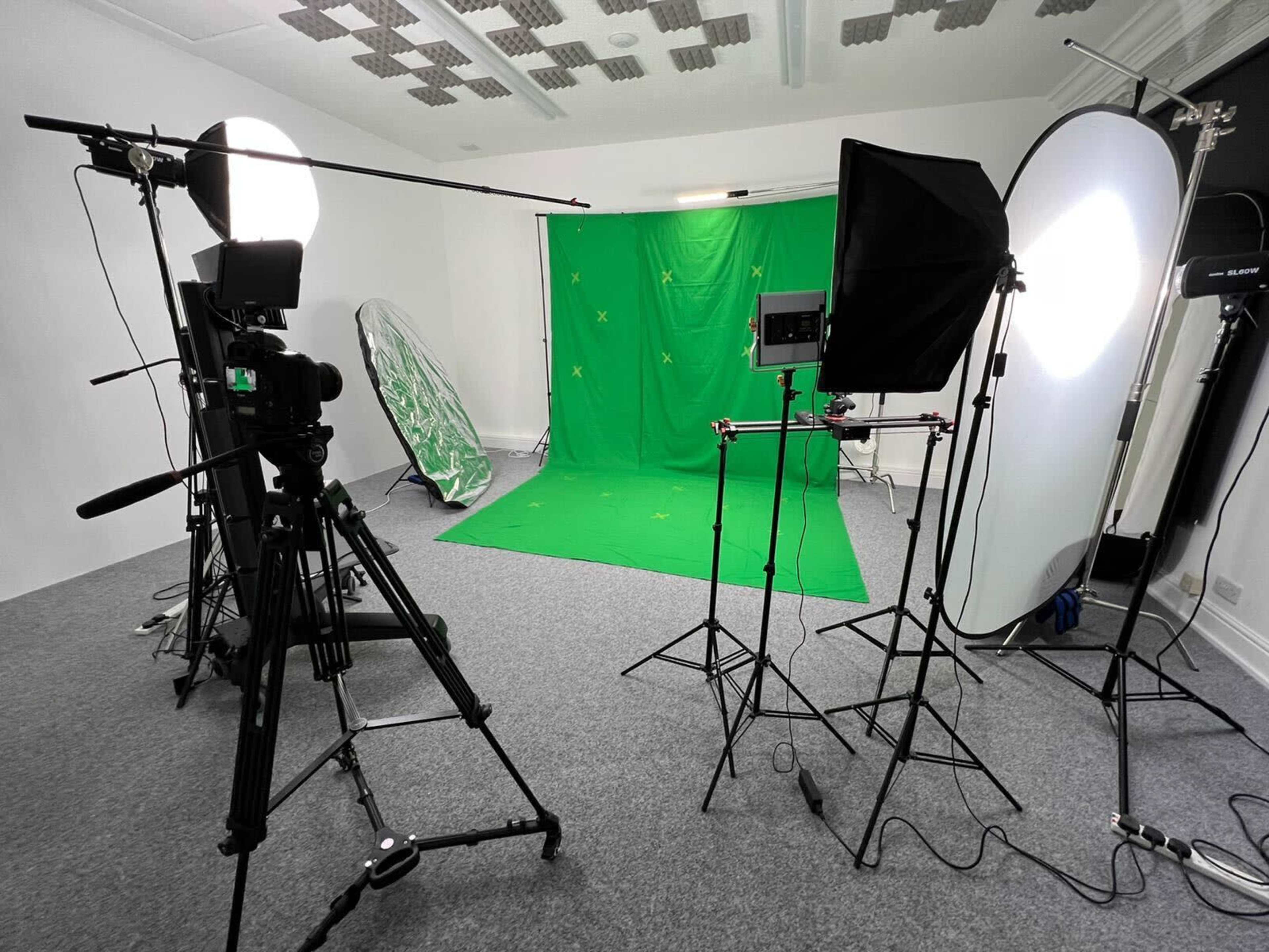 A photography studio set up with a green backdrop, tripods, and lighting equipment arranged for a video or photo shoot.