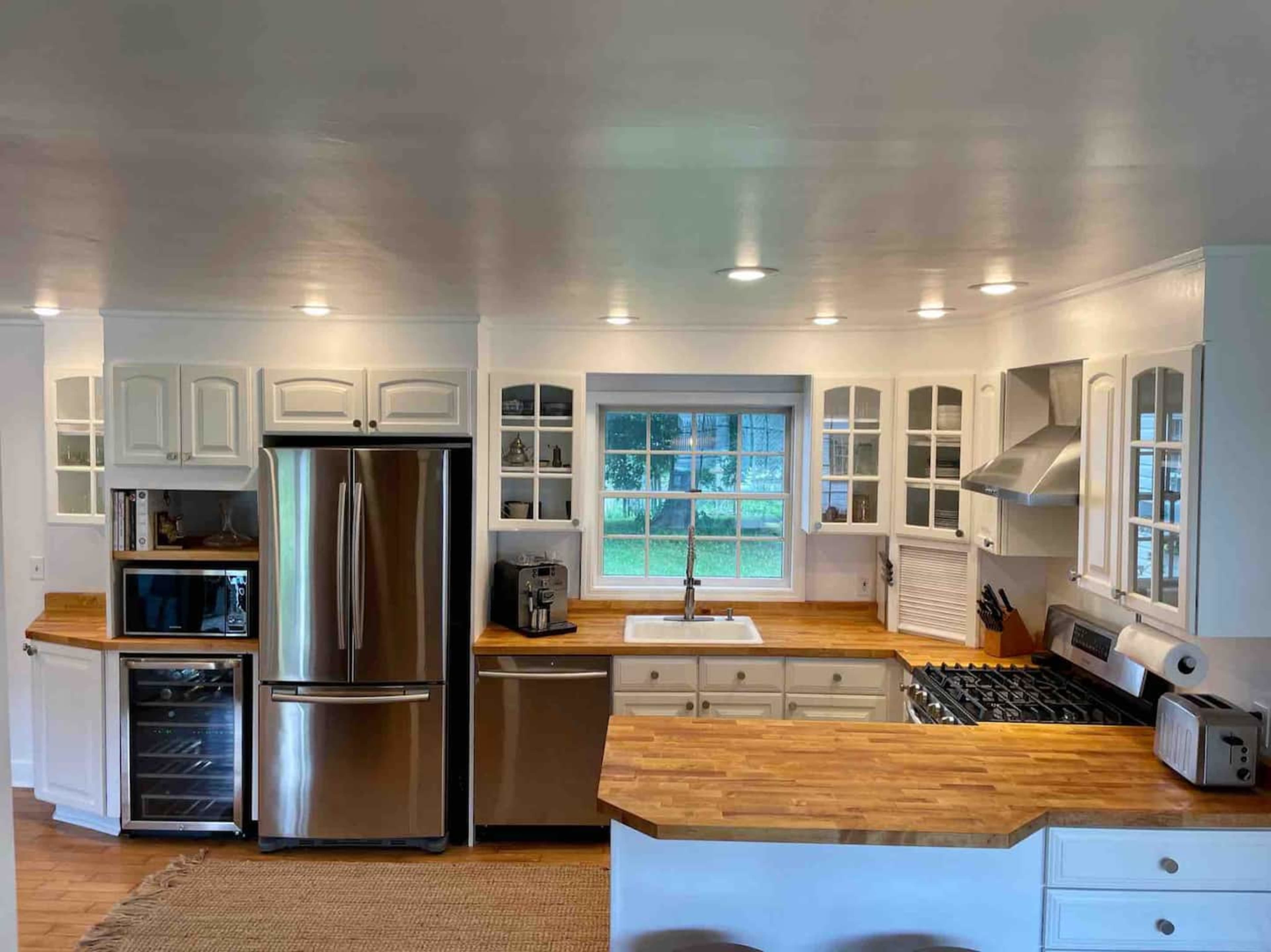 A modern kitchen features white cabinetry, a stainless steel refrigerator, and a central island with a wooden countertop.