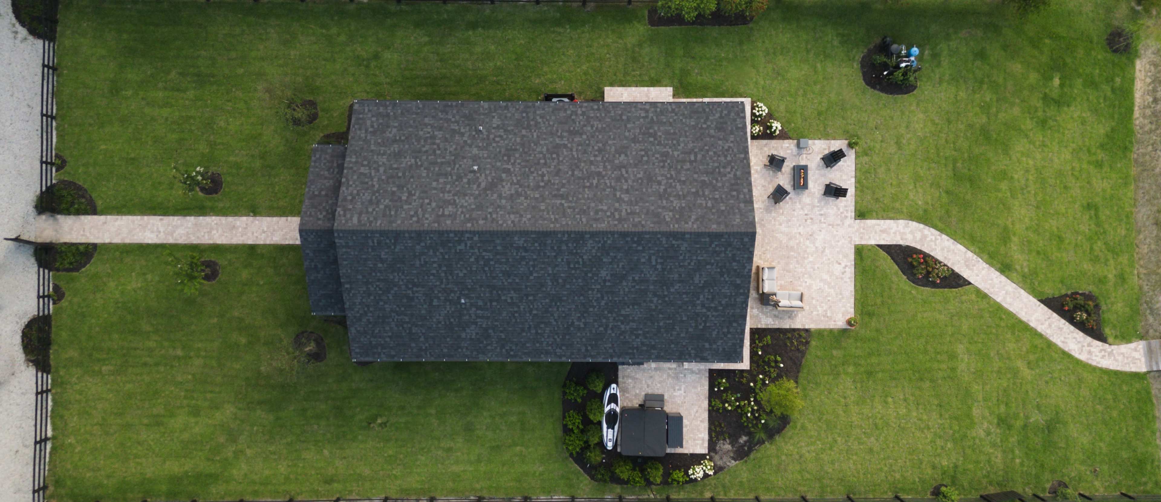 An aerial view of a house surrounded by a well-manicured lawn and a stone pathway leading to a patio with seating.