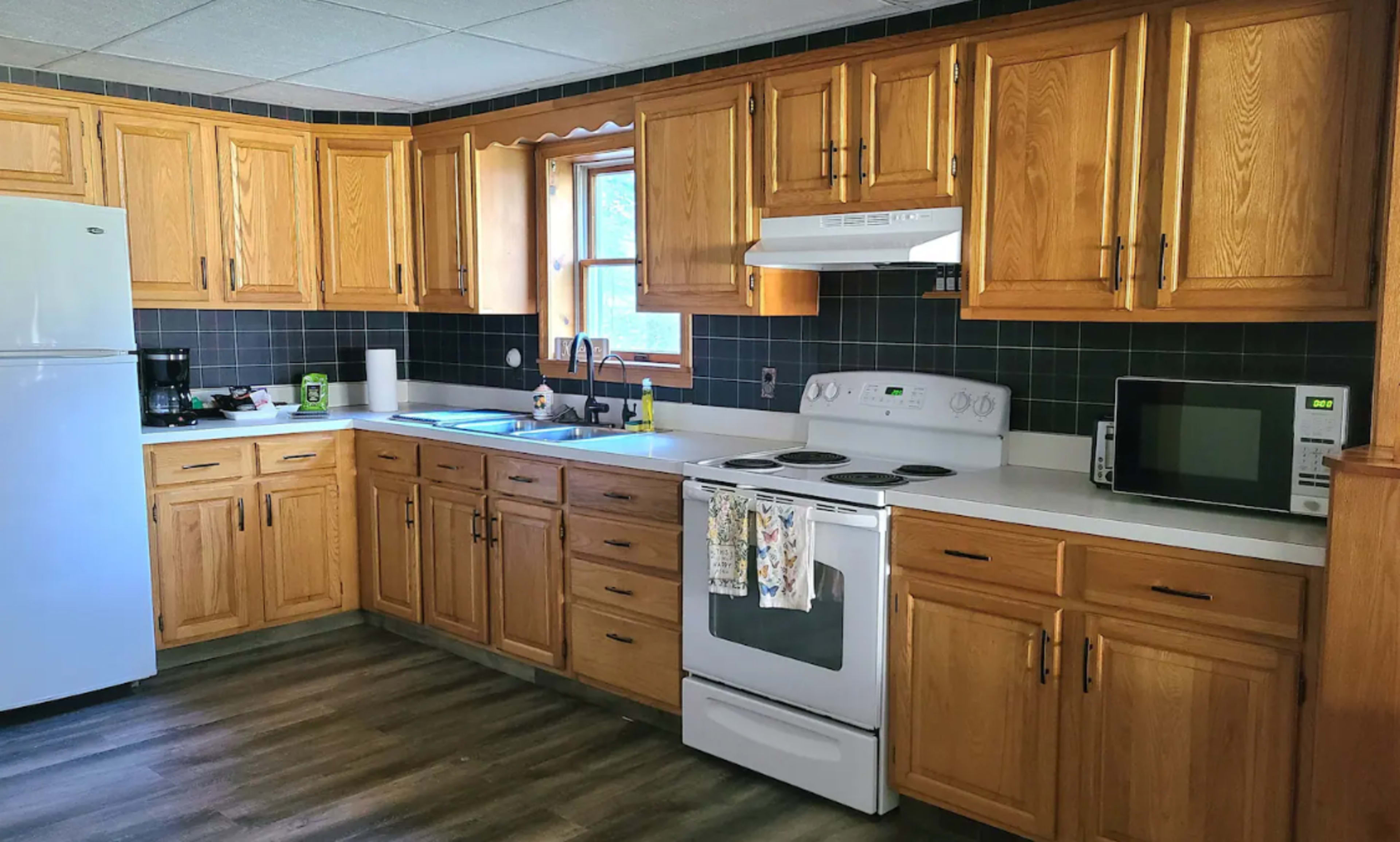 A kitchen with wooden cabinets, a white stove, a microwave, and a sink under a window.