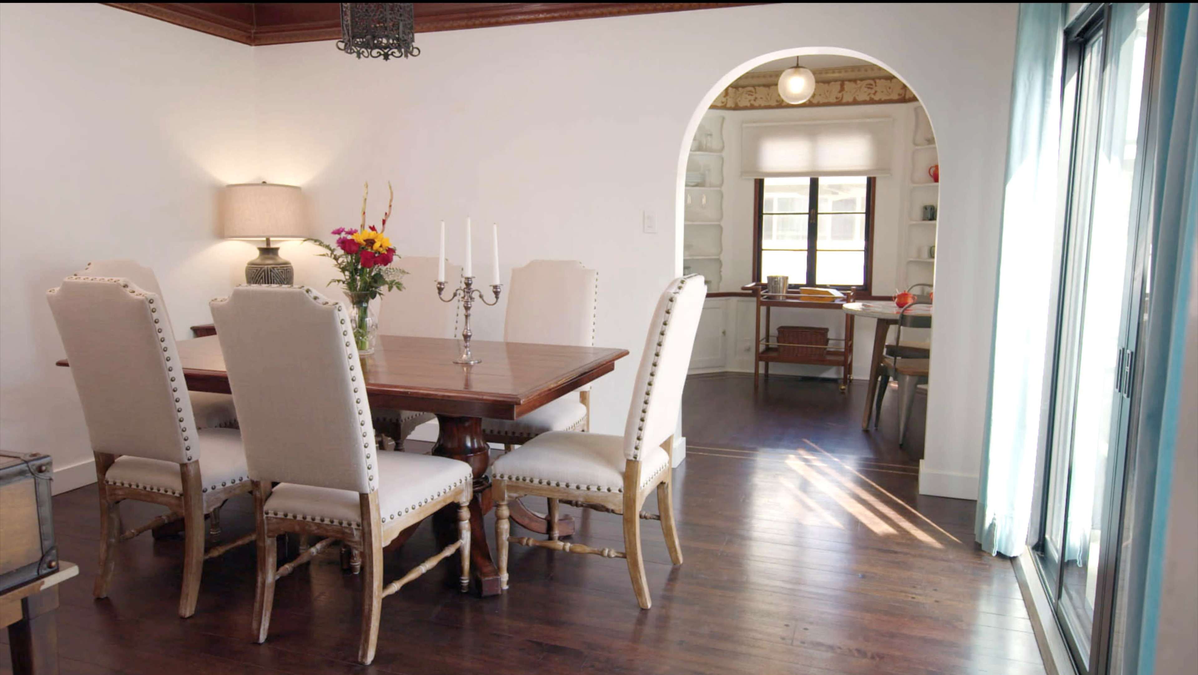 A dining room features a wooden table surrounded by upholstered chairs, with a bouquet of flowers and a candelabra as centerpieces.