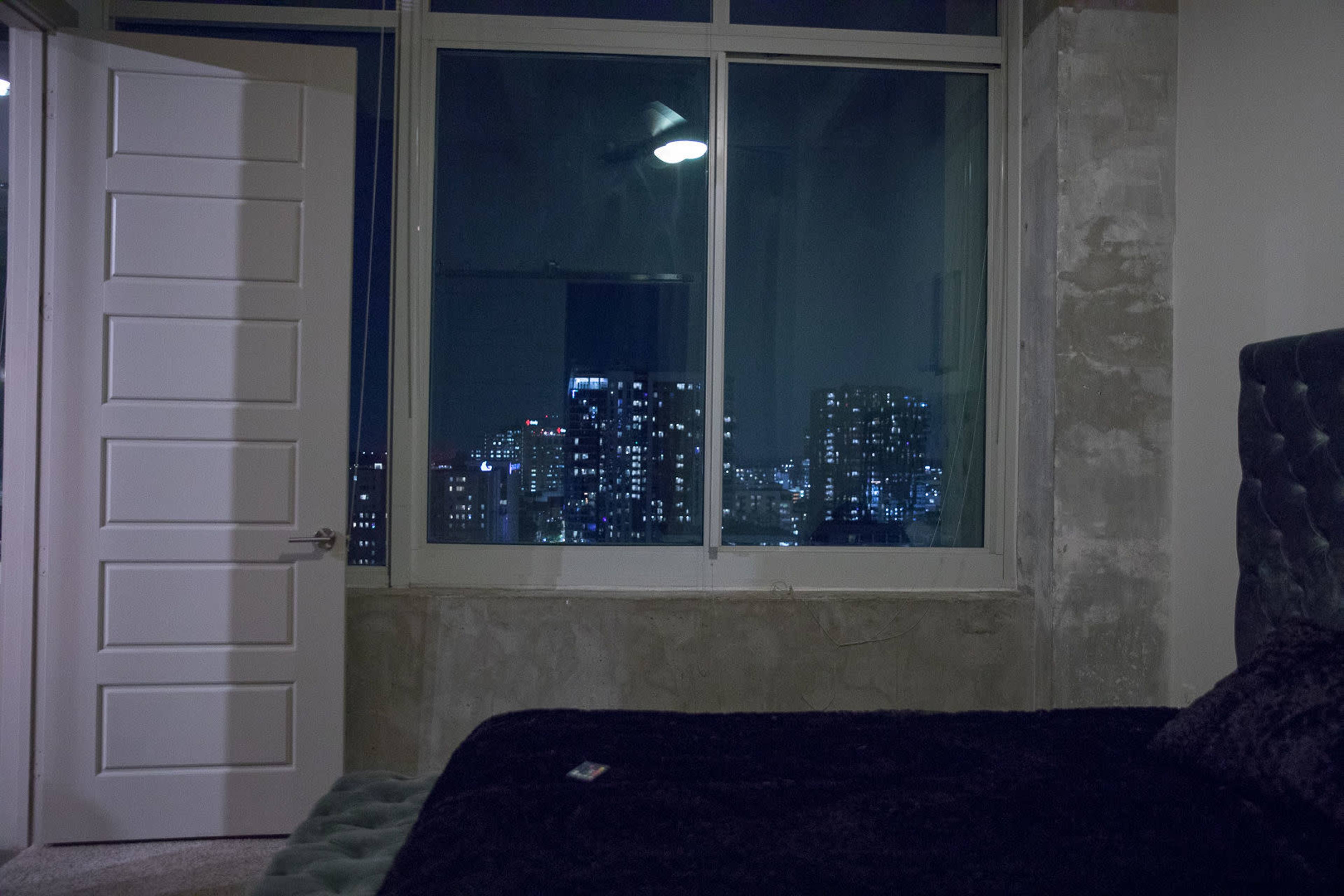 A bedroom with a large window showcases a nighttime city skyline filled with lights.